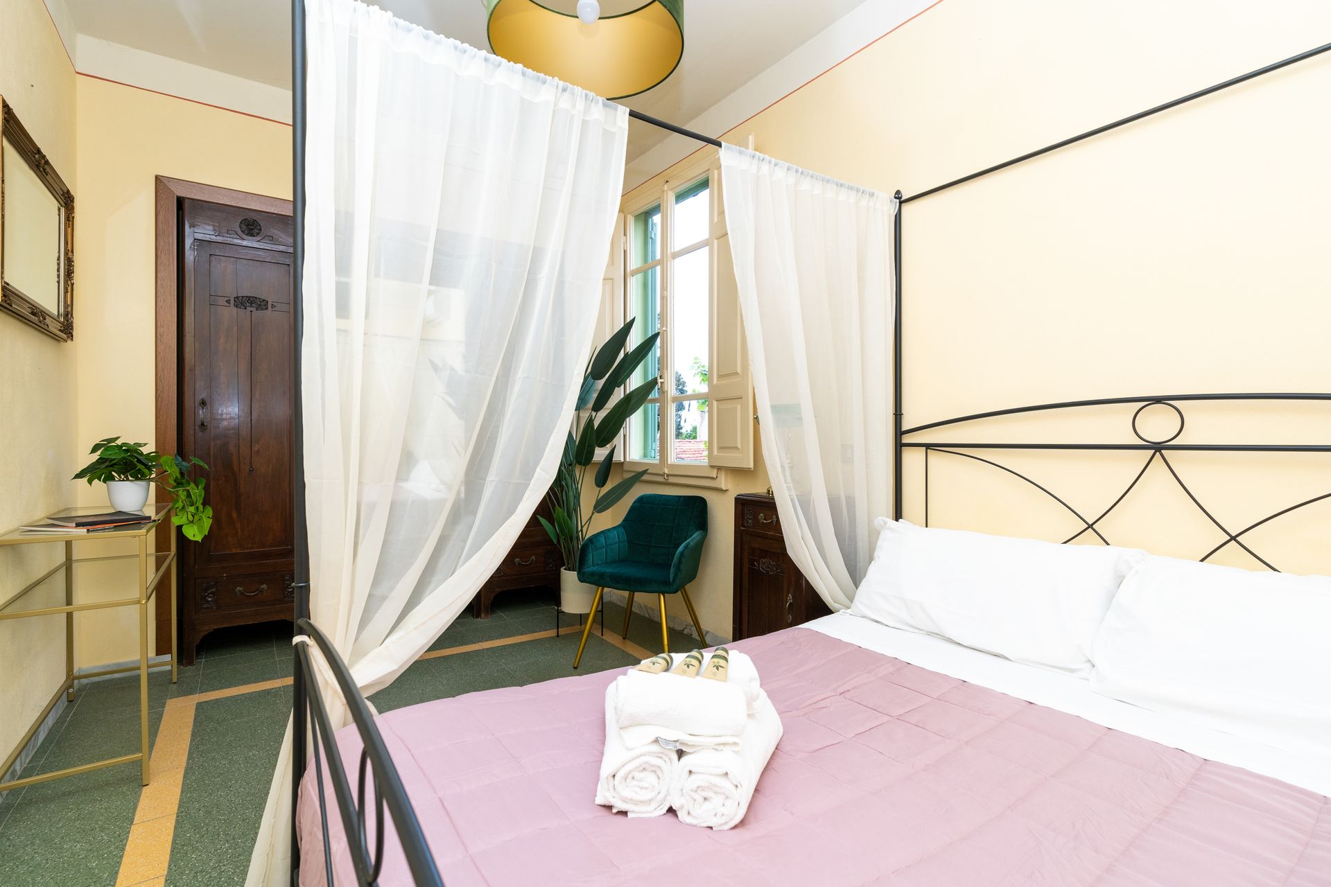 Bedroom with a canopy bed, sheer curtains, a green velvet chair by the window.