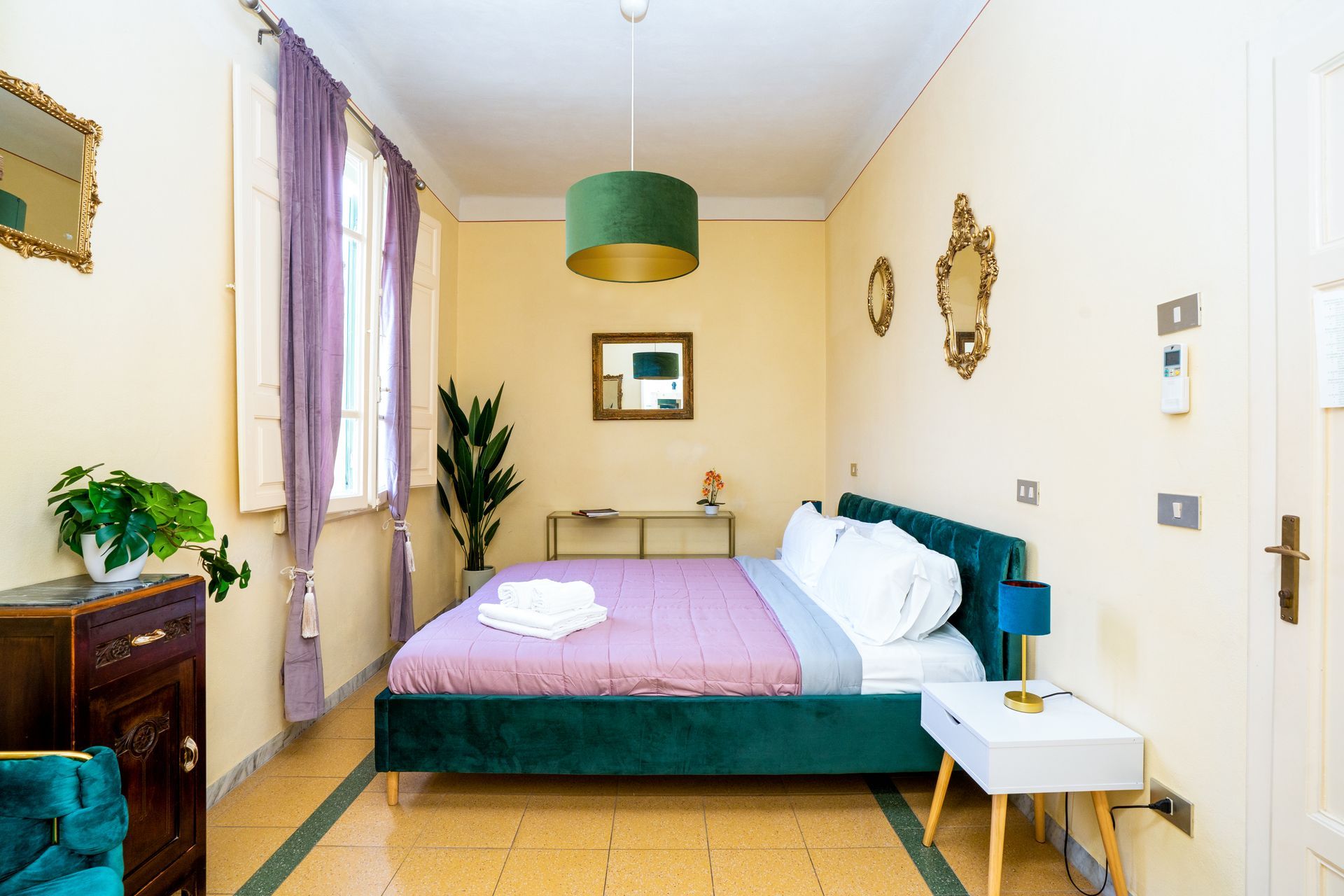 Bedroom with a green bed, purple curtains, and gold-framed mirrors. Light-colored walls and flooring.