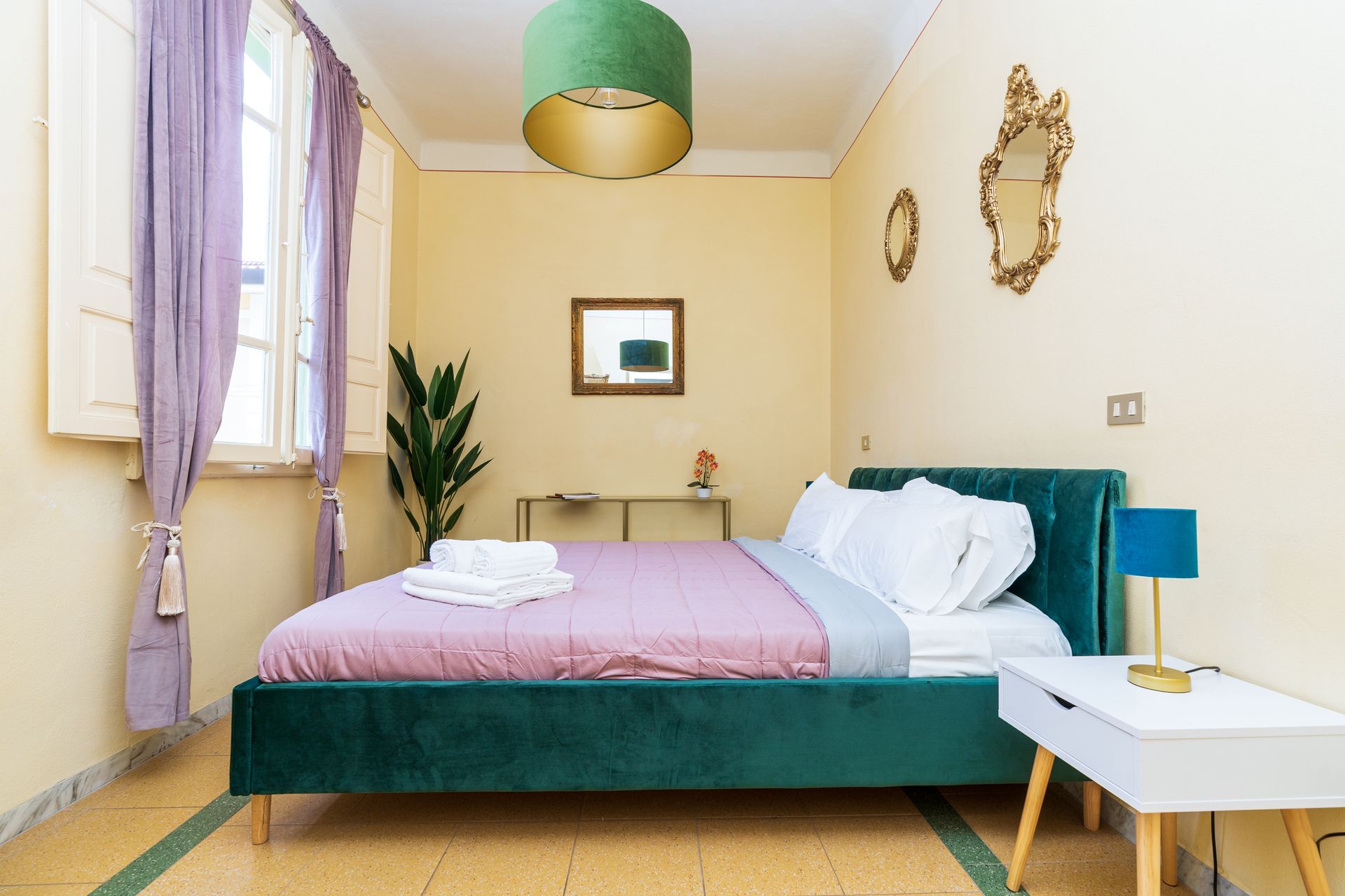 Bedroom with a green bed, purple curtains, and gold-framed mirrors on a yellow wall.