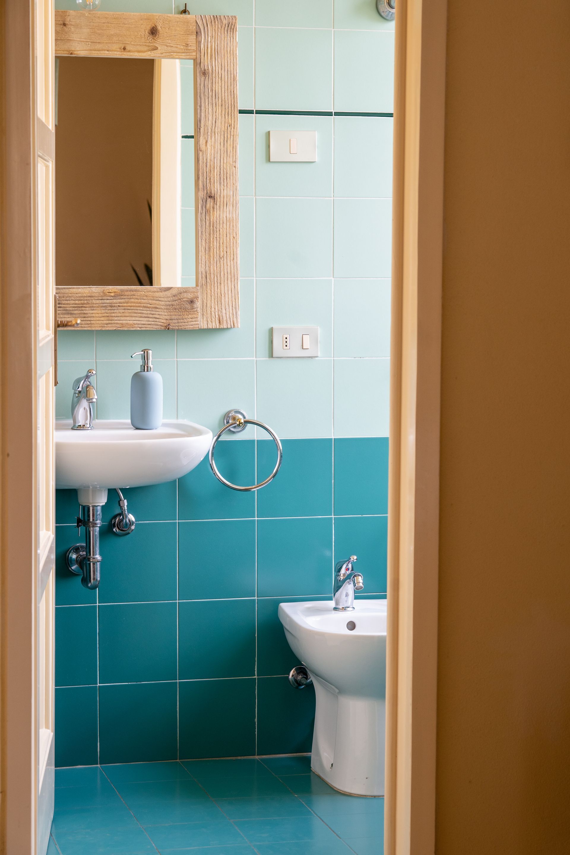 Bathroom with turquoise and light blue tiles, sink, bidet, and wooden-framed mirror.