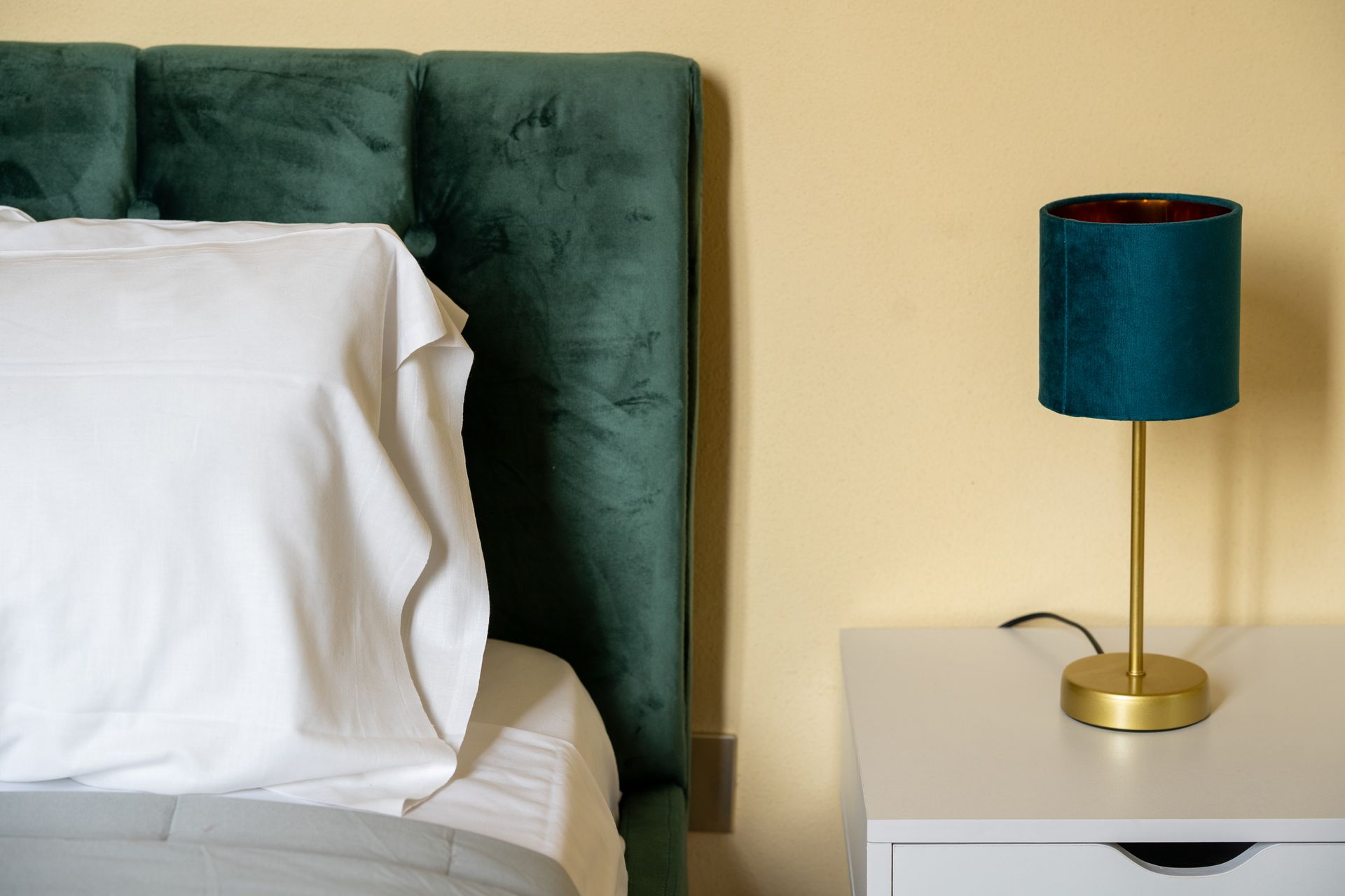 Bed with green headboard and white pillow, bedside table with teal lamp.