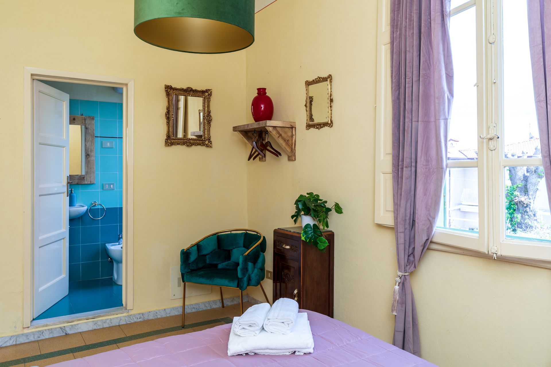 Bedroom with open door to a blue bathroom, green chair, purple curtains, and a window.