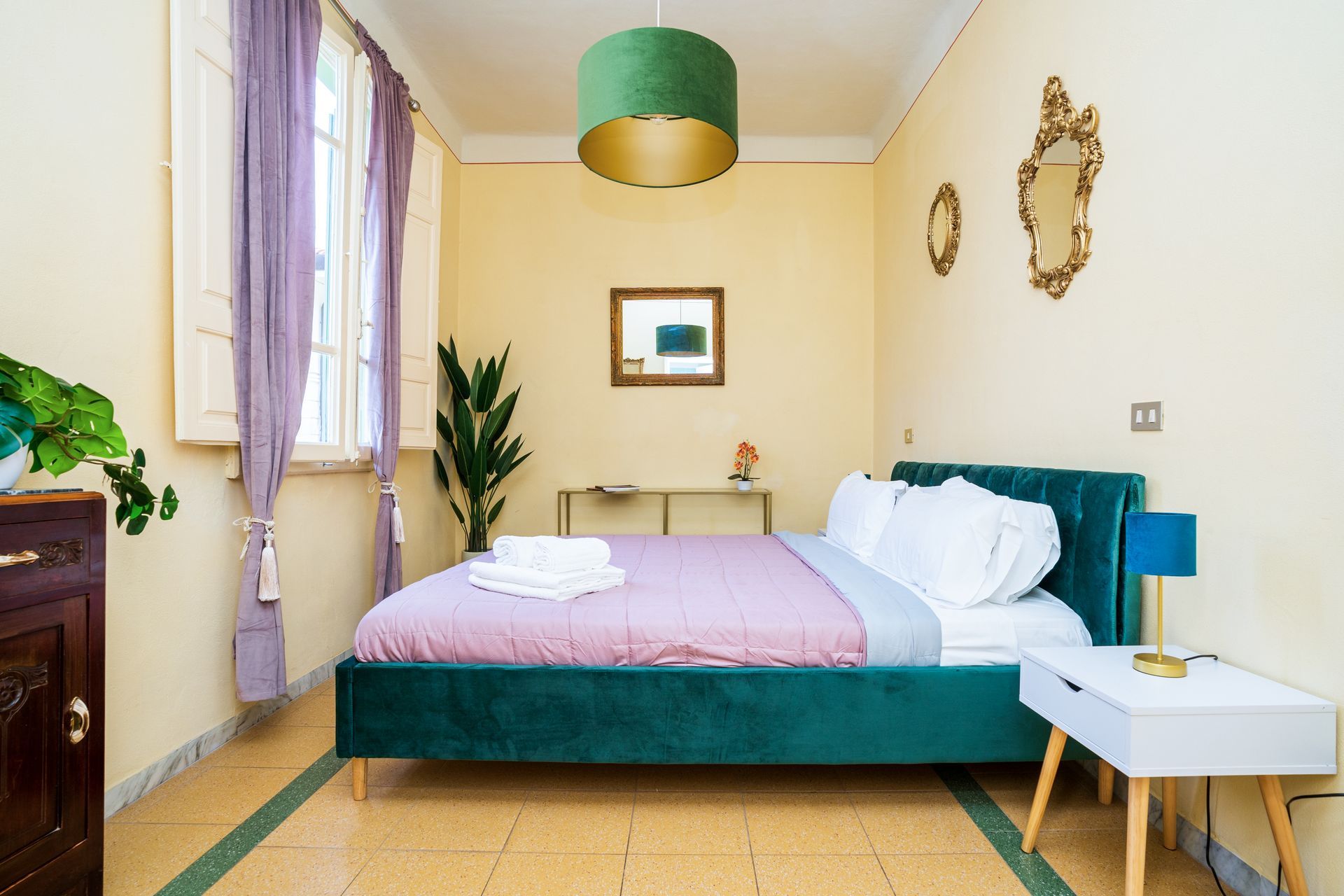Bedroom with green bed, purple curtains, gold accents, and a white nightstand.