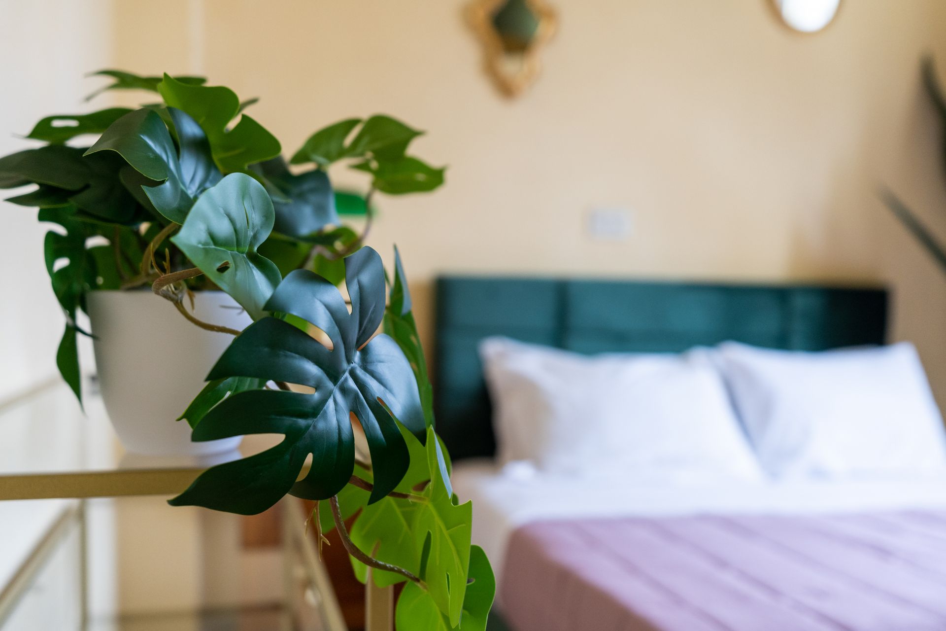 A potted plant sits on a shelf in front of a bed with white pillows and a green headboard.
