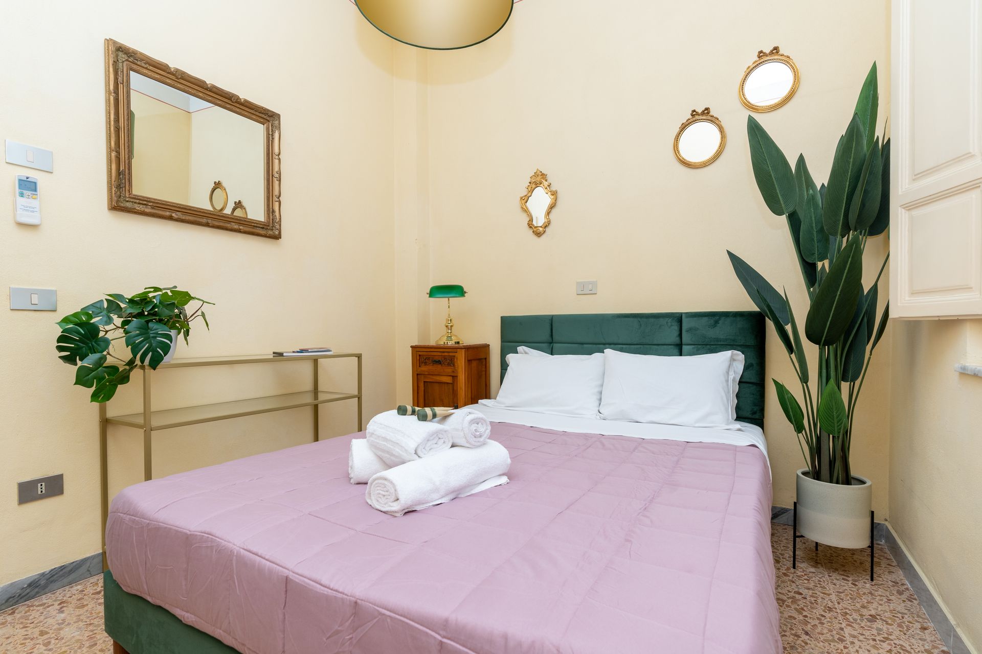 Bedroom with a bed, mirror, plant, and nightstand; walls are yellow.