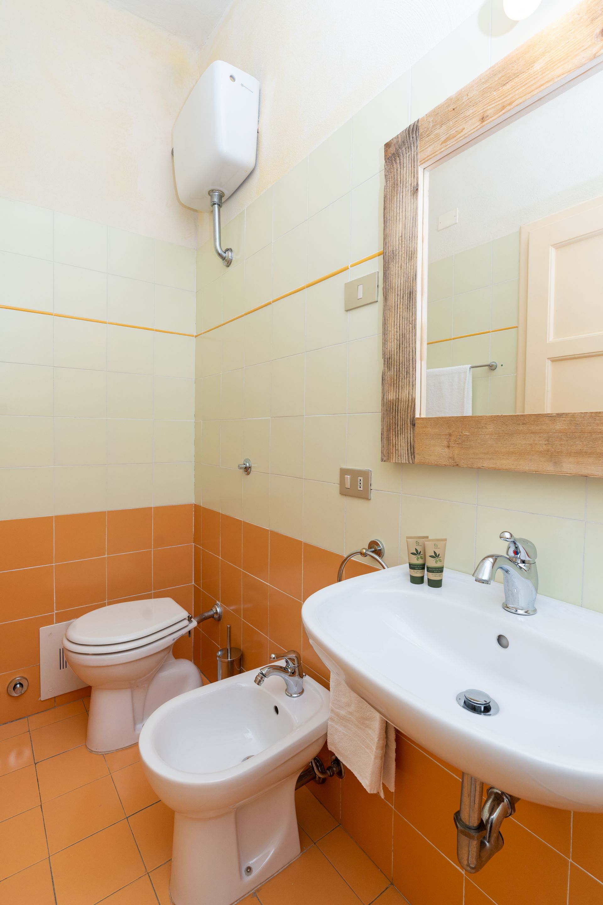Bathroom with white fixtures, orange and white tiled walls, and a wooden mirror frame.