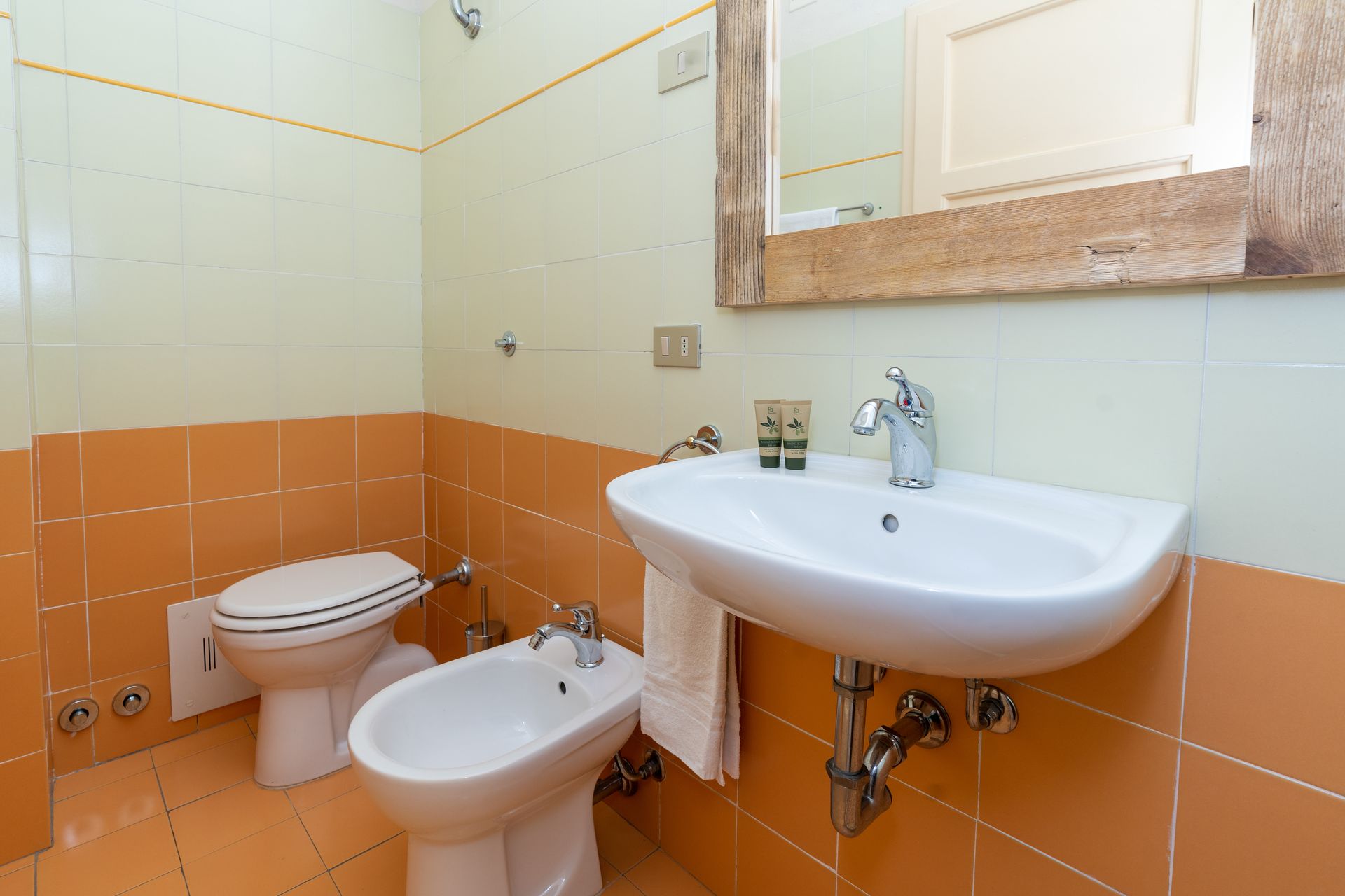 Bathroom with white fixtures, orange and white tiled walls, and a wooden-framed mirror.