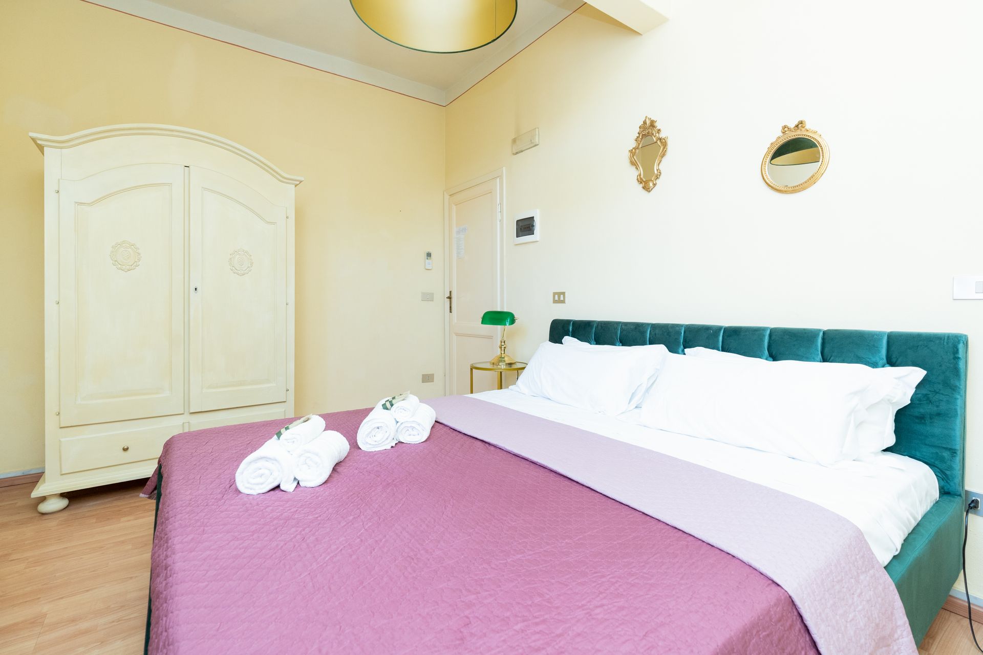 Bedroom with teal headboard, purple bedspread, white wardrobe, and gold accents.