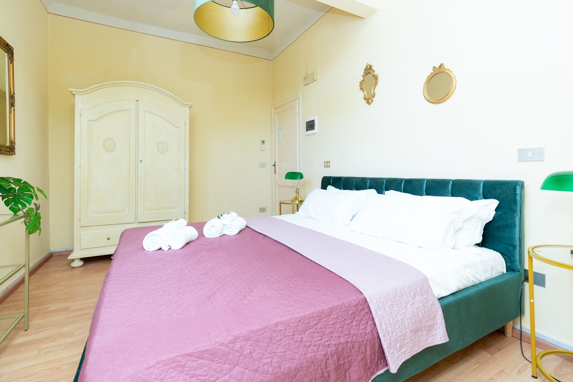Bedroom with a green velvet bed, white wardrobe, and gold accents.