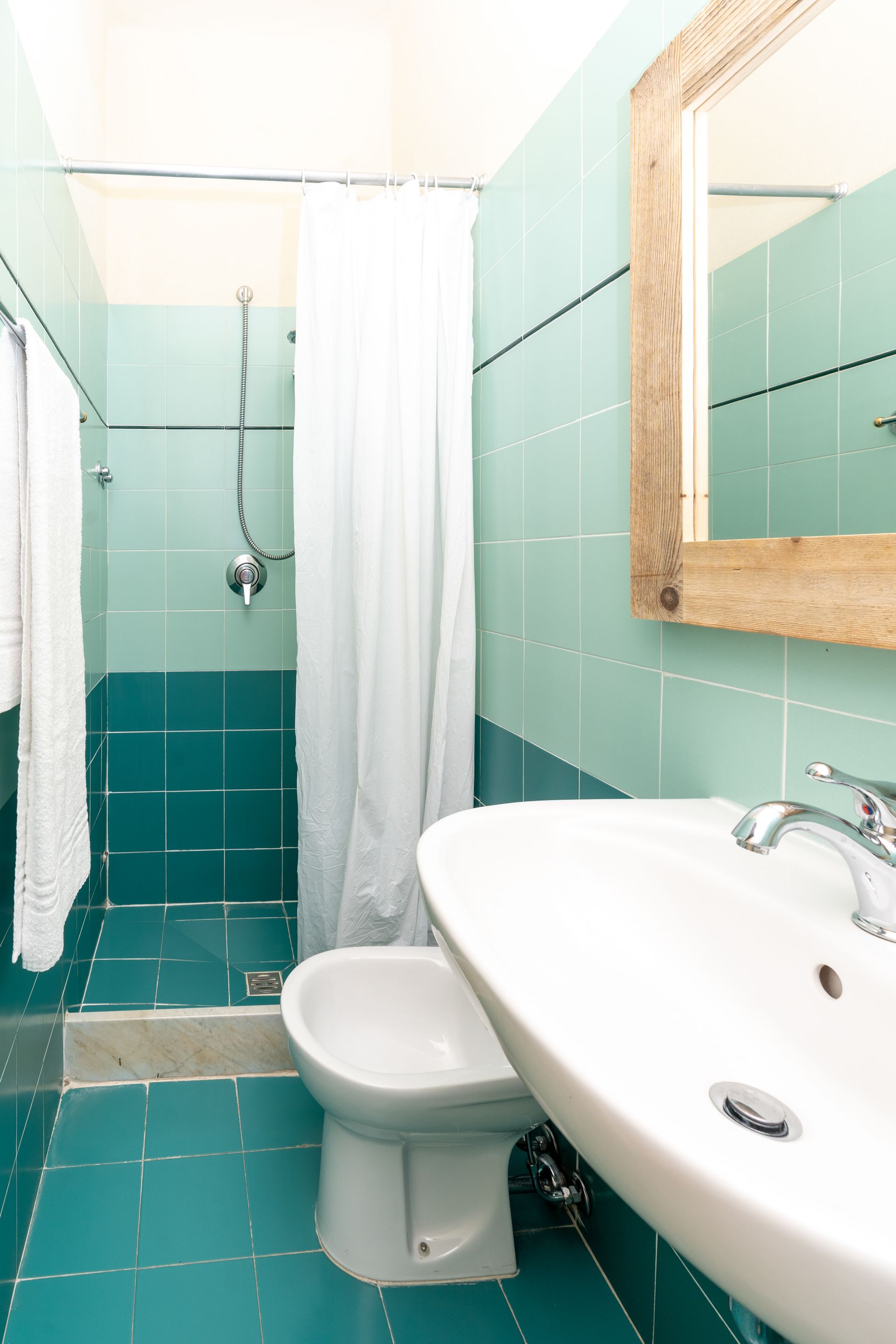 Bathroom with turquoise tile, shower, sink, bidet, and wooden-framed mirror.