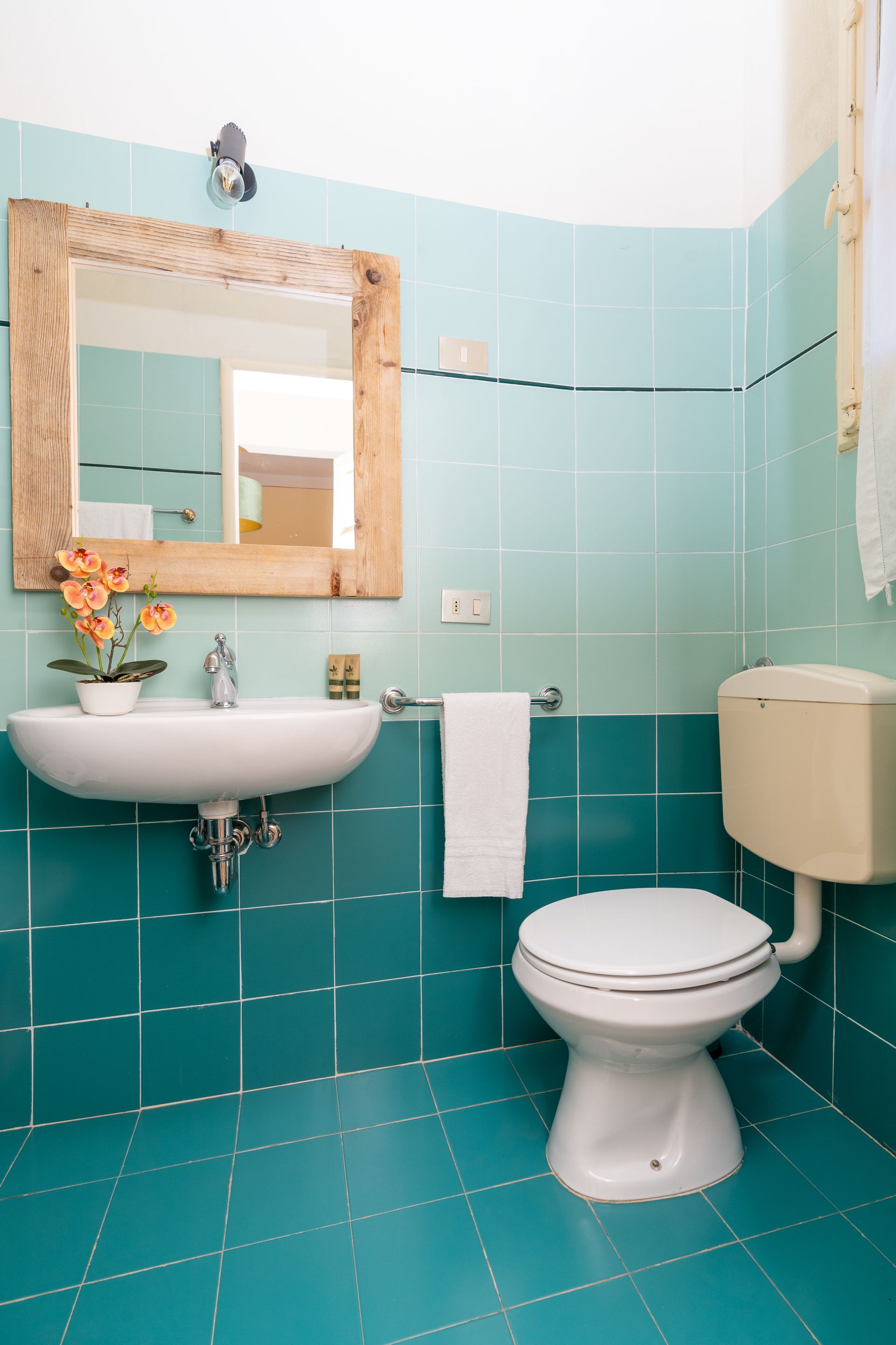 Small bathroom with teal tile, sink, toilet, and mirror with a wooden frame.