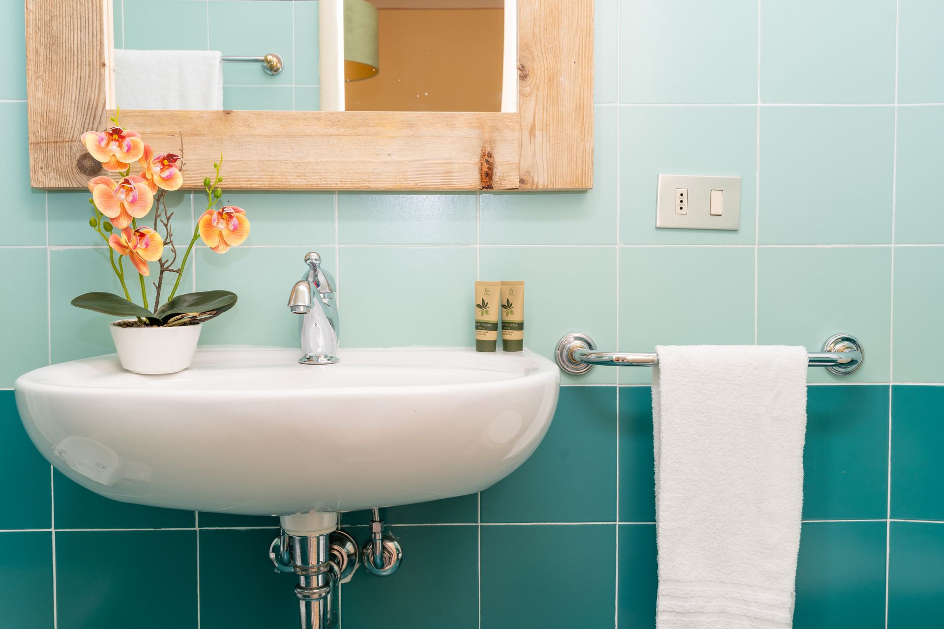 Bathroom sink with turquoise tile, a decorative flower, and a hanging towel.