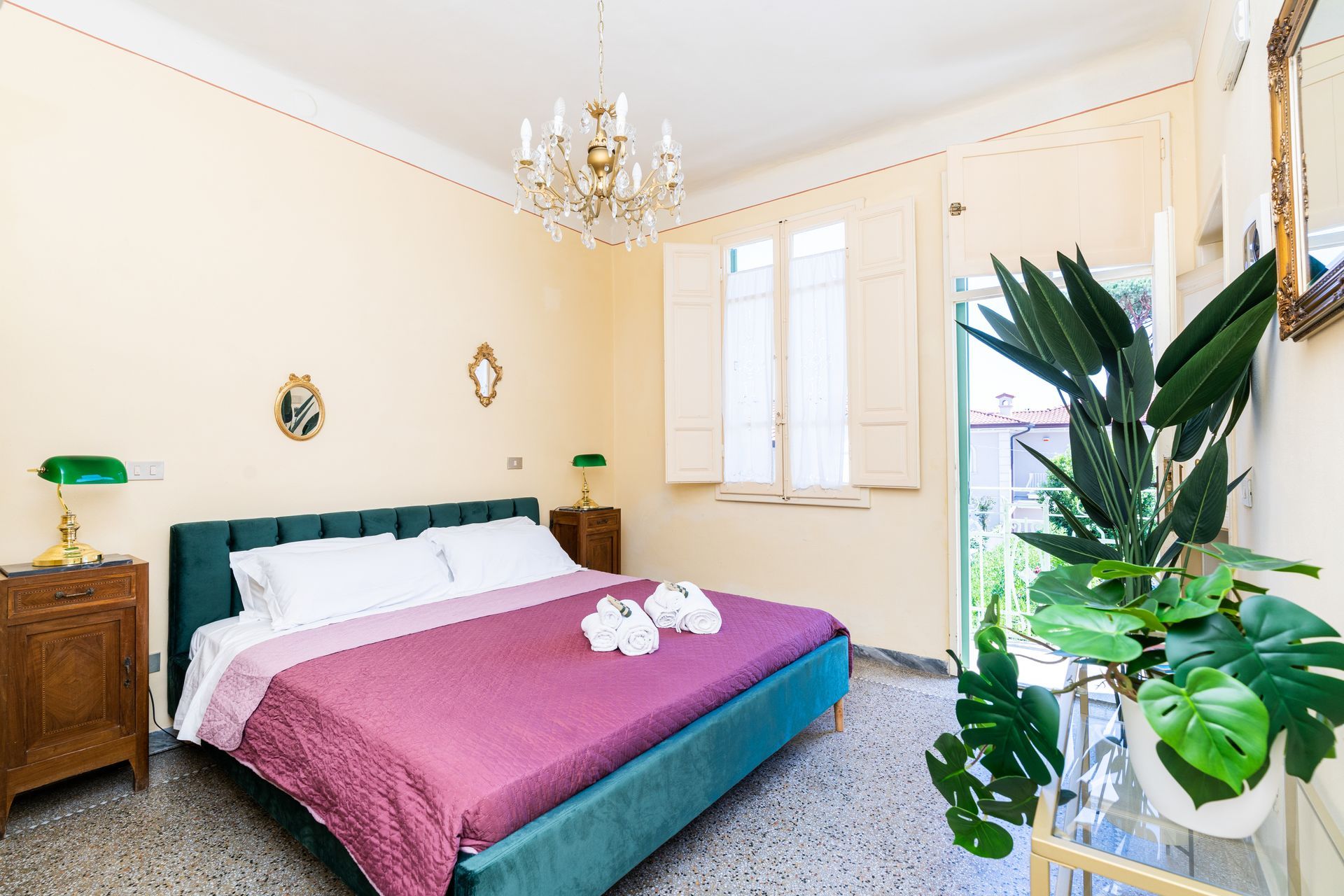Bedroom with teal bed, purple blanket, ornate chandelier, and potted plants.