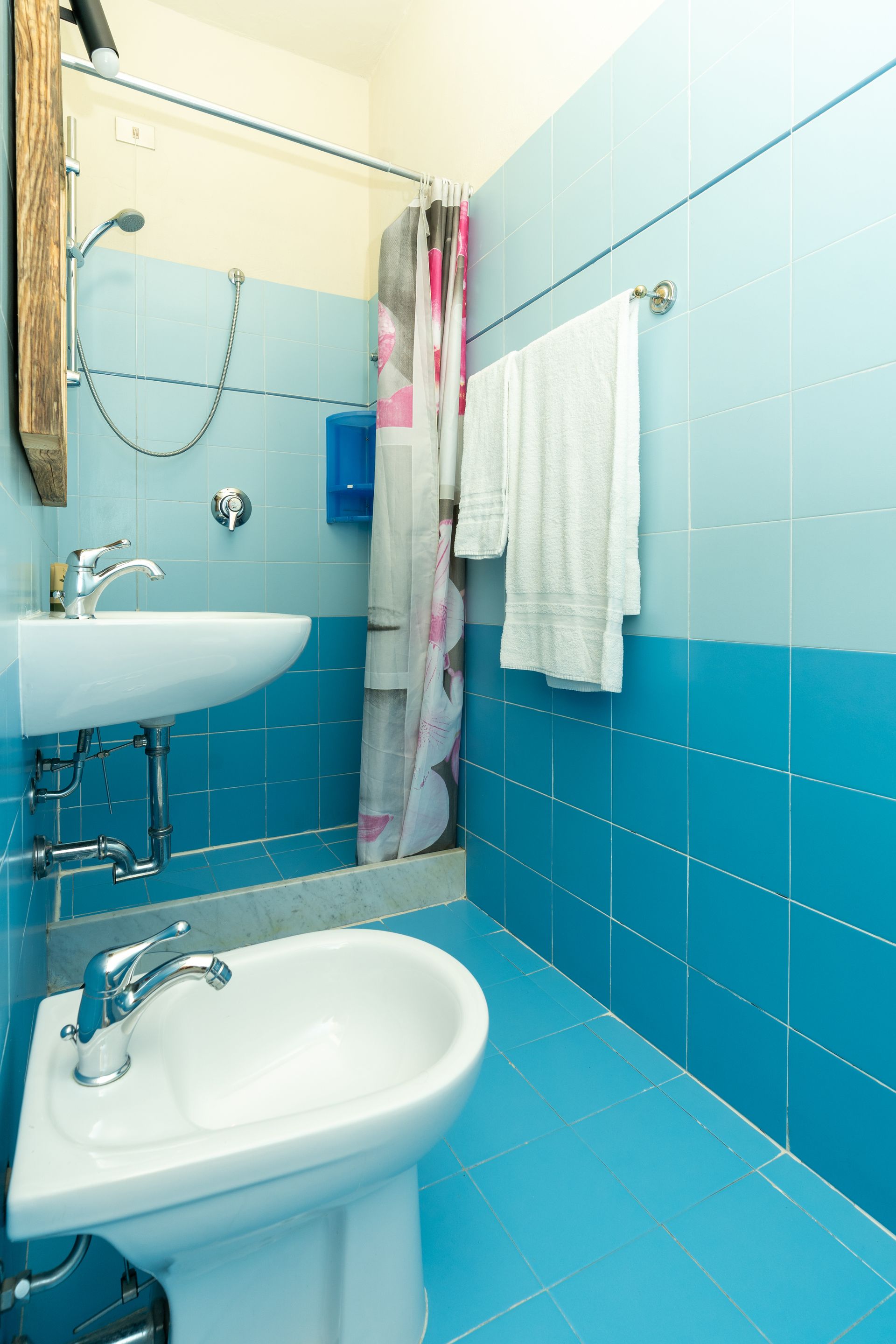 Small blue tiled bathroom with sink, bidet, shower, and towel rack.