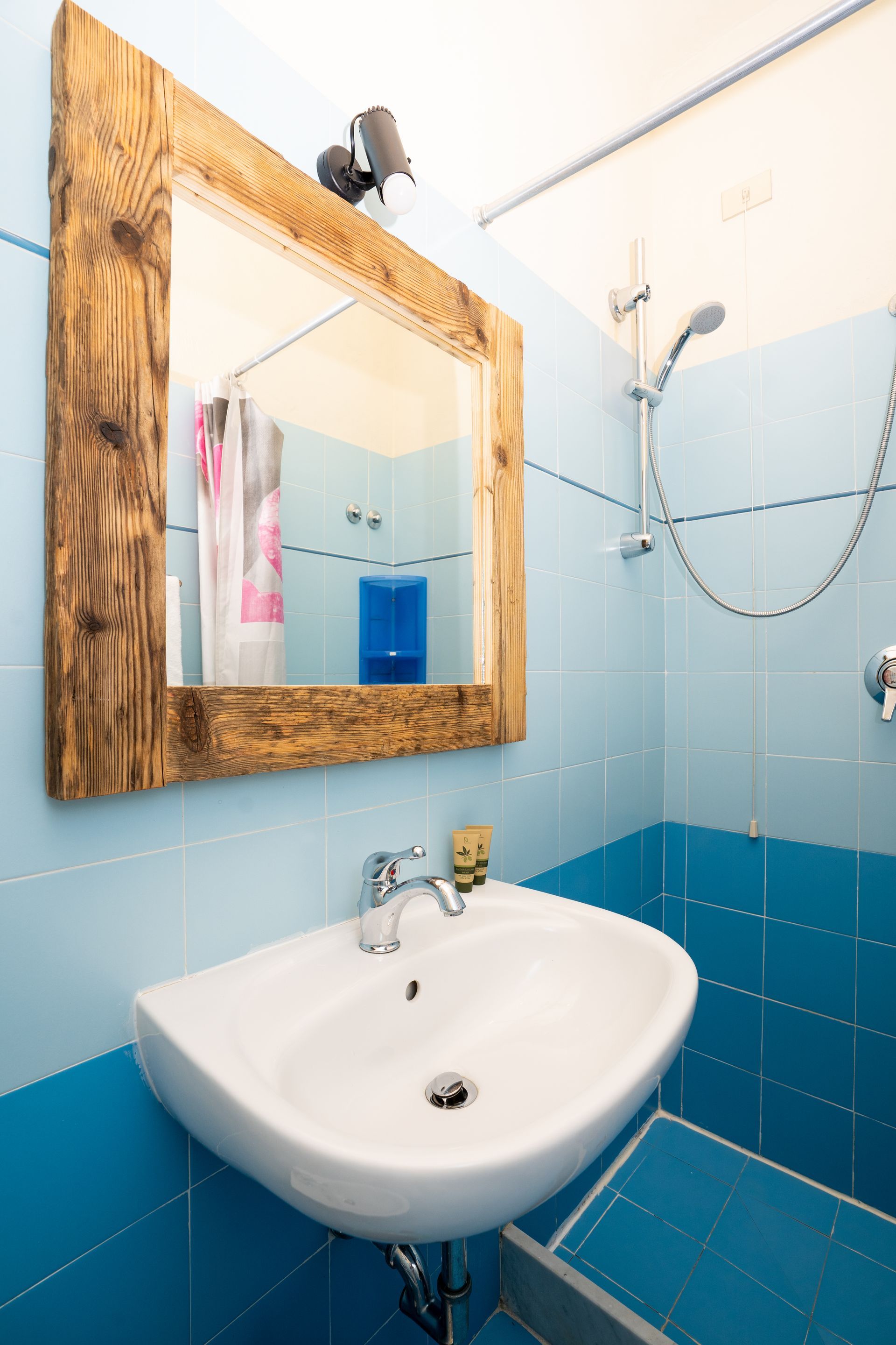Small blue-tiled bathroom with a white sink, large wooden-framed mirror, and shower.