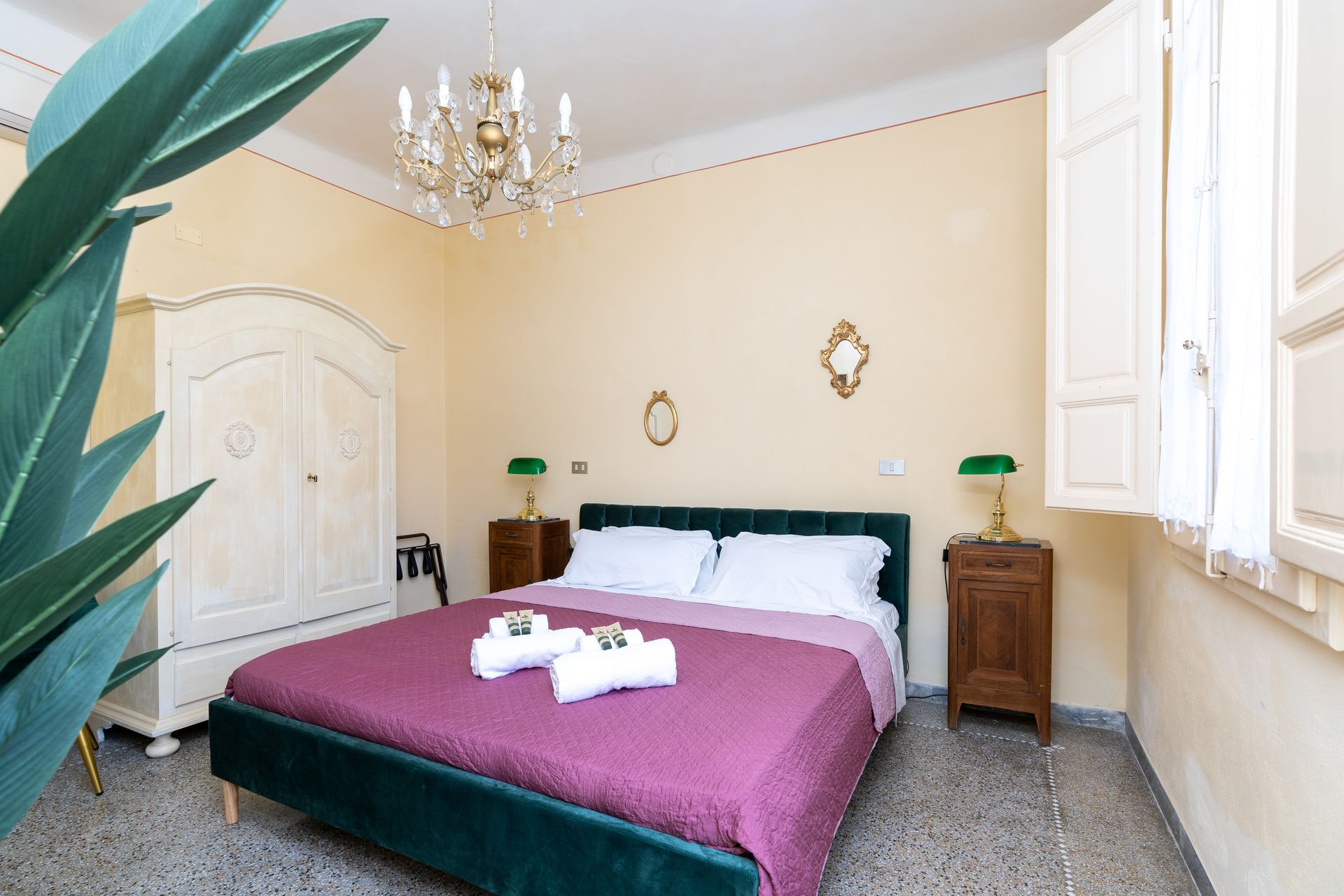 Bedroom with double bed, wardrobe, nightstands, chandelier, and a large plant.