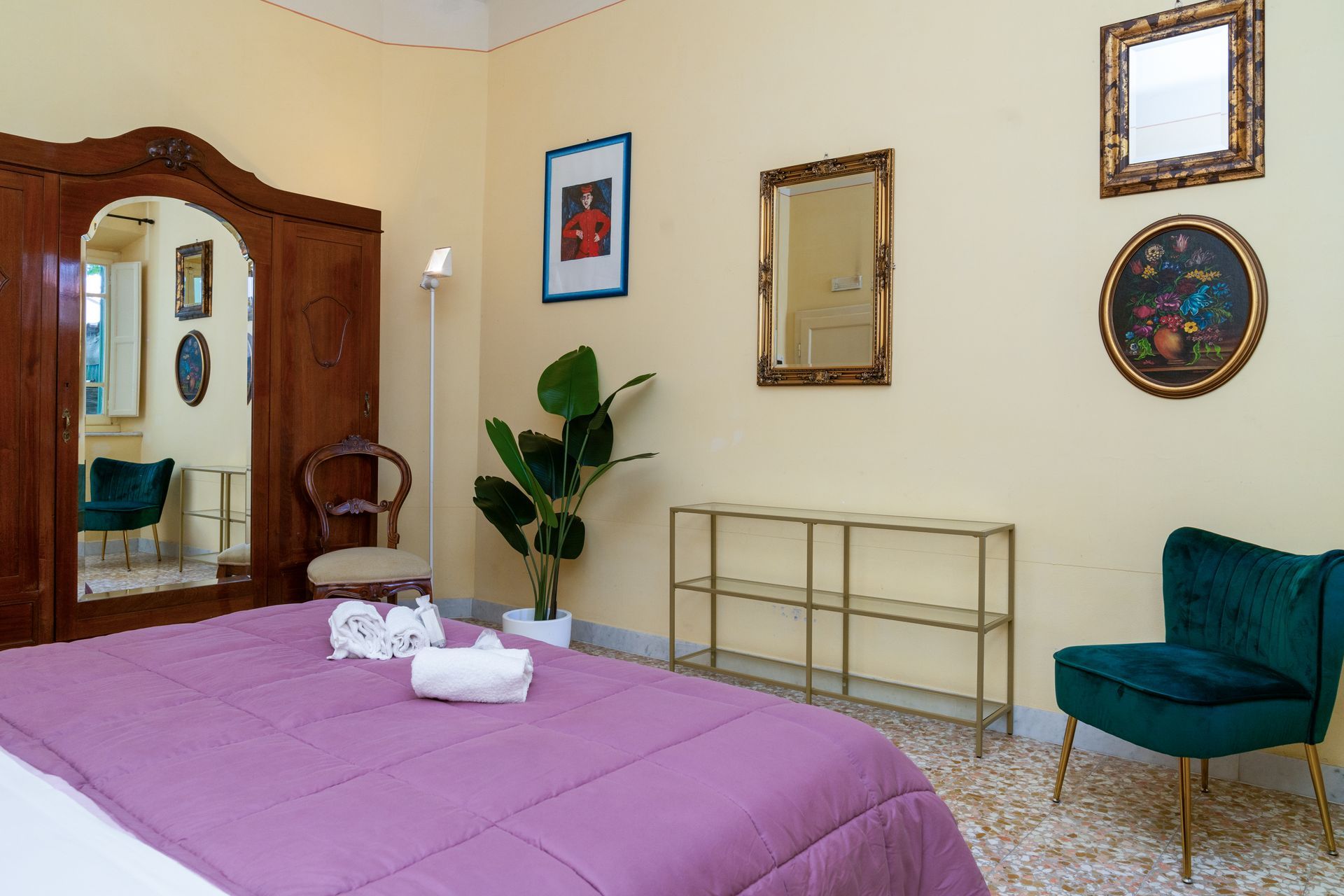 Bedroom with a purple bedspread, a tall wooden wardrobe, and green velvet chair.