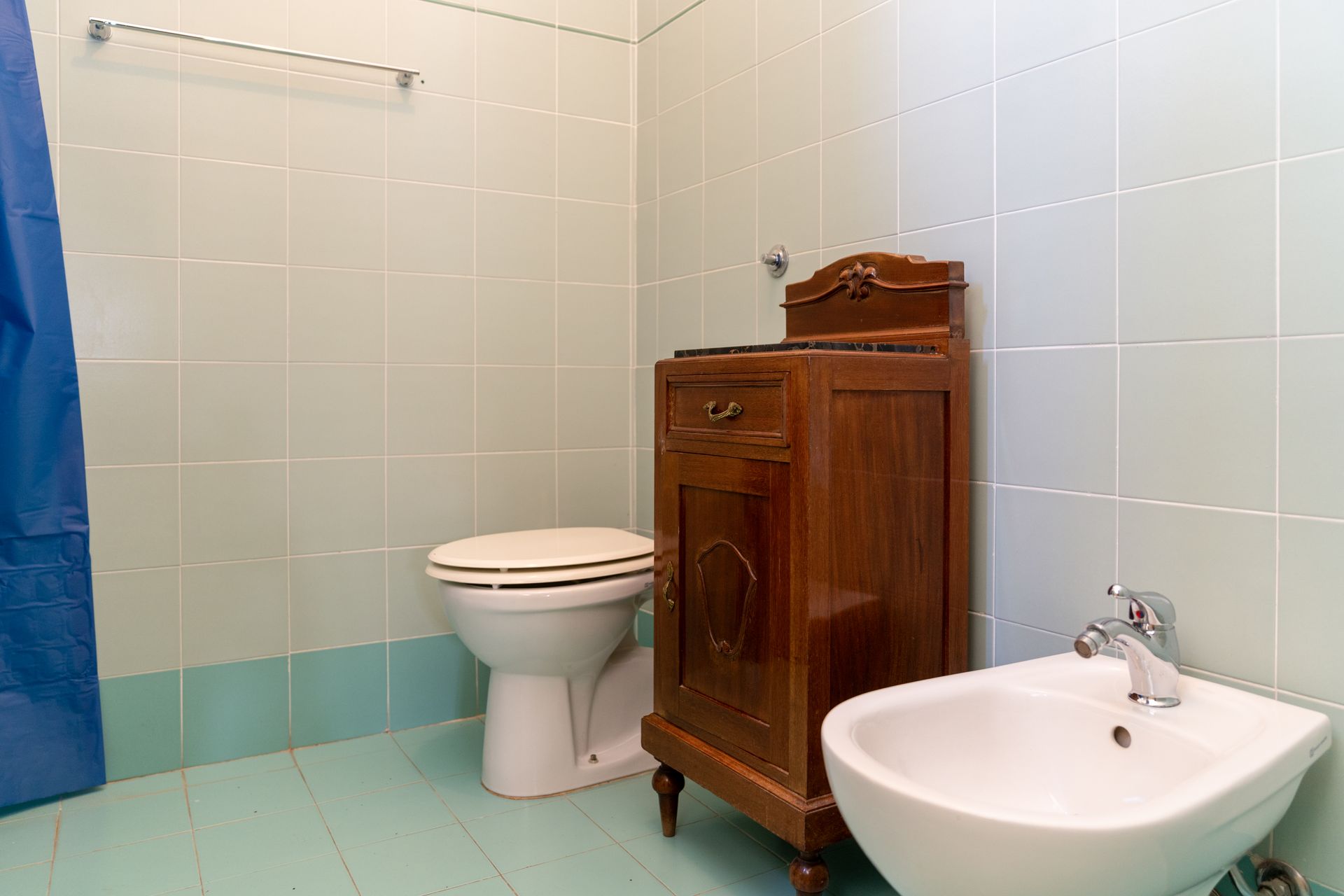 Bathroom with toilet, bidet, and wooden cabinet. Blue and light green tiled walls and floor.