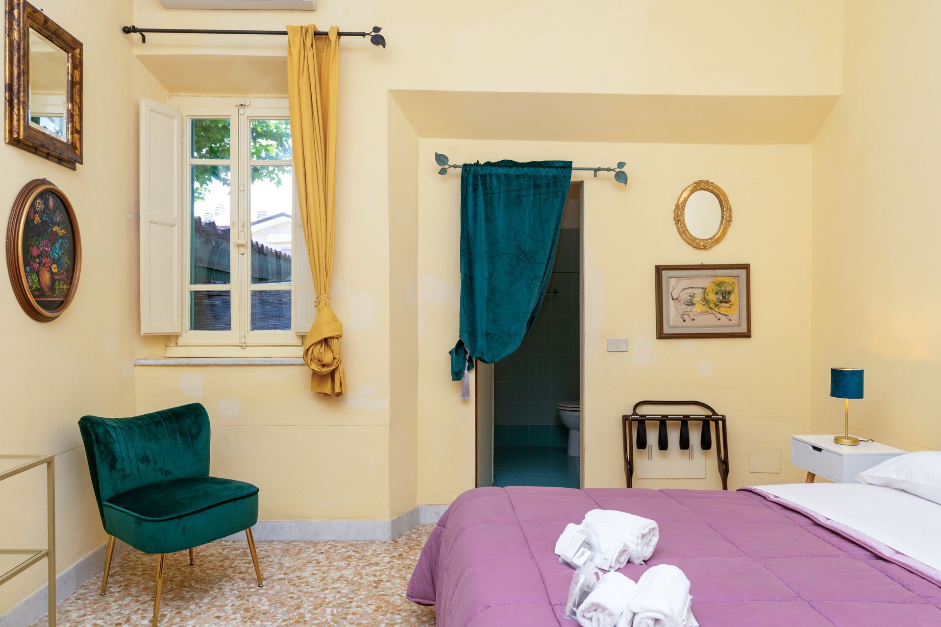 Bedroom with teal chair, purple bedspread, yellow walls, and framed art. Window with yellow curtain.