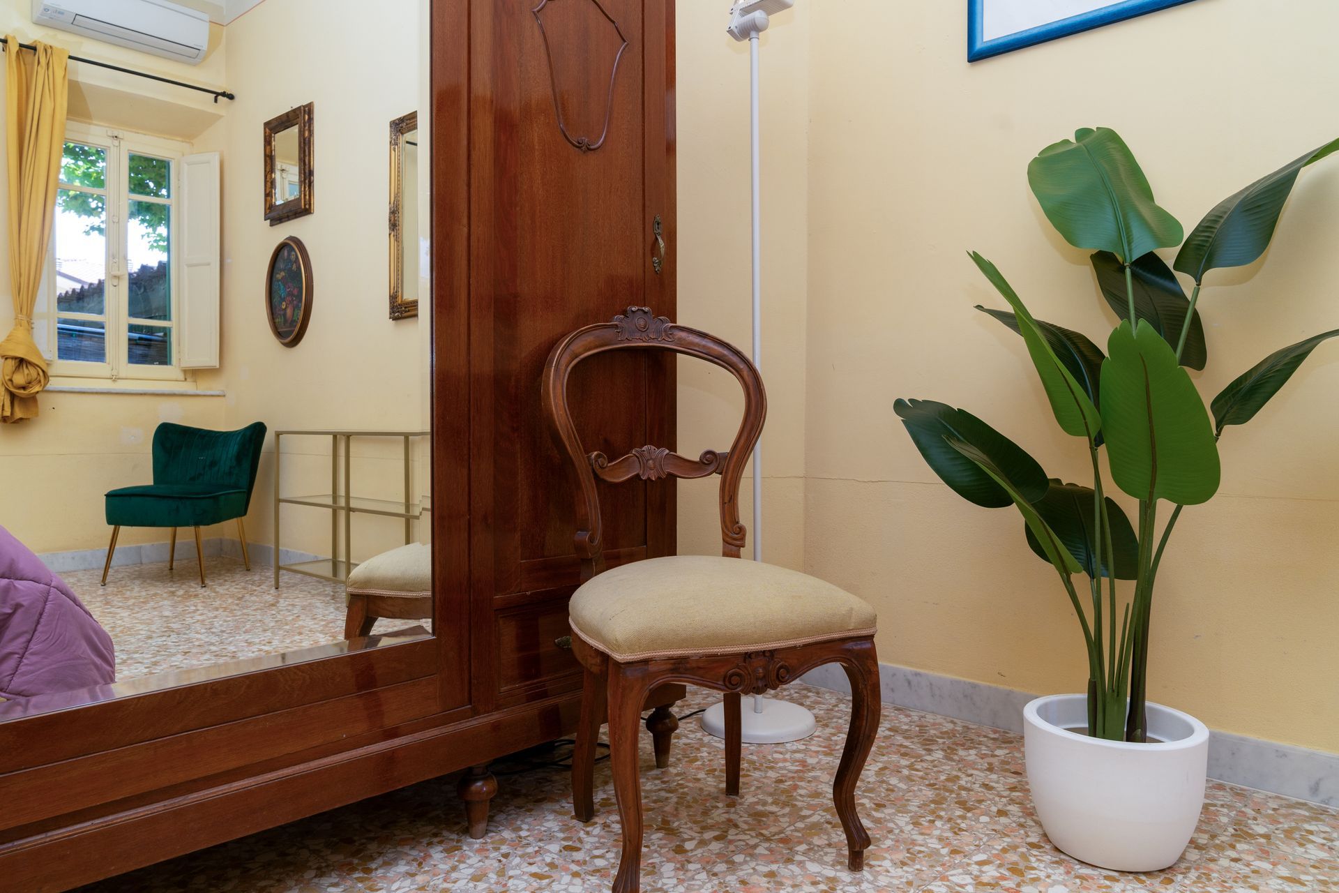 Bedroom with antique furniture: large wooden wardrobe, ornate chair, green armchair, potted plant.