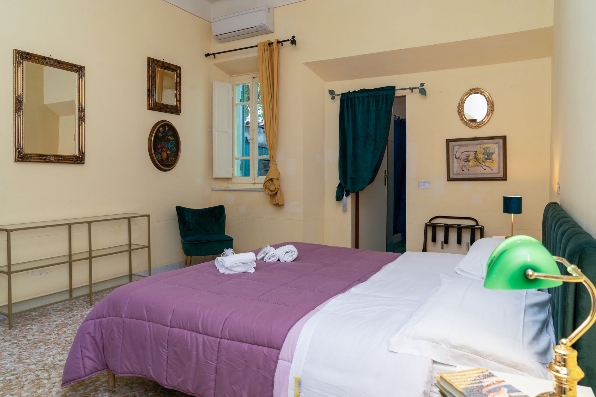 Bedroom with a purple bedspread, various mirrors, a chair, and a green lamp.