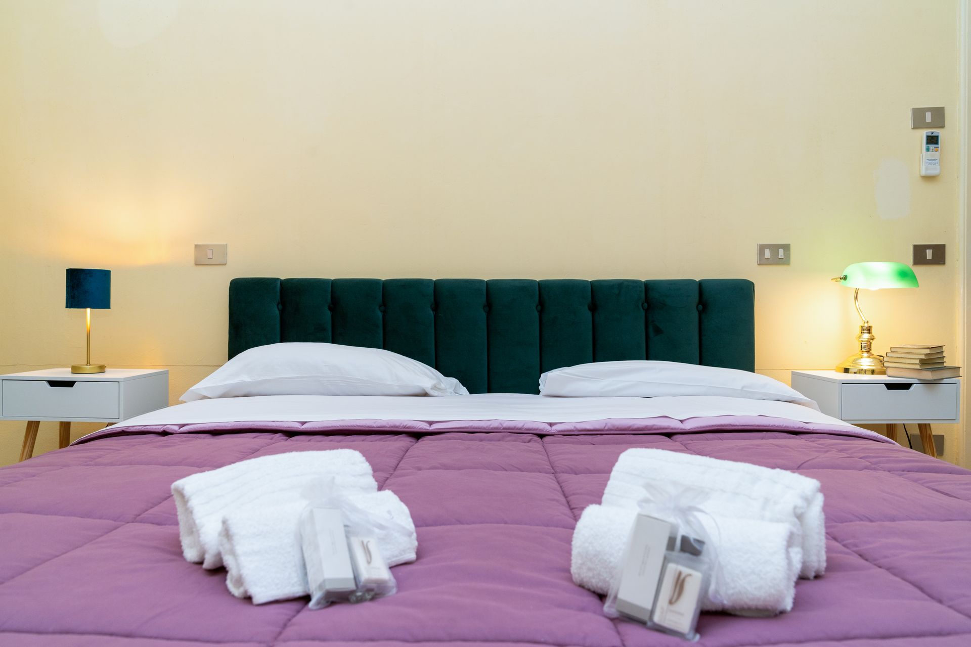 A bedroom with a bed covered in a purple comforter, two nightstands, and lamps.