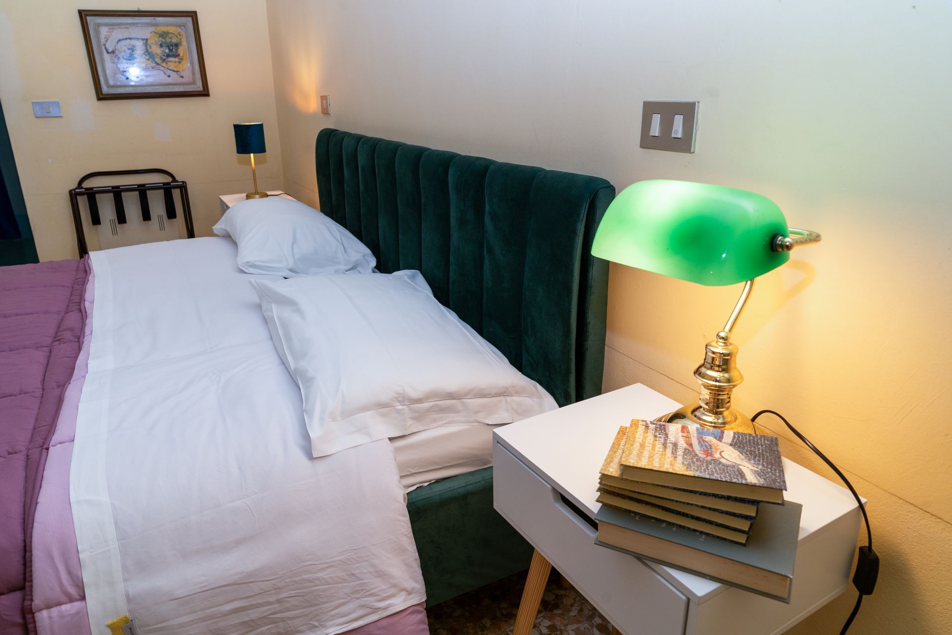 Bedroom with green velvet headboard, white bedding, and a green desk lamp on a white nightstand.