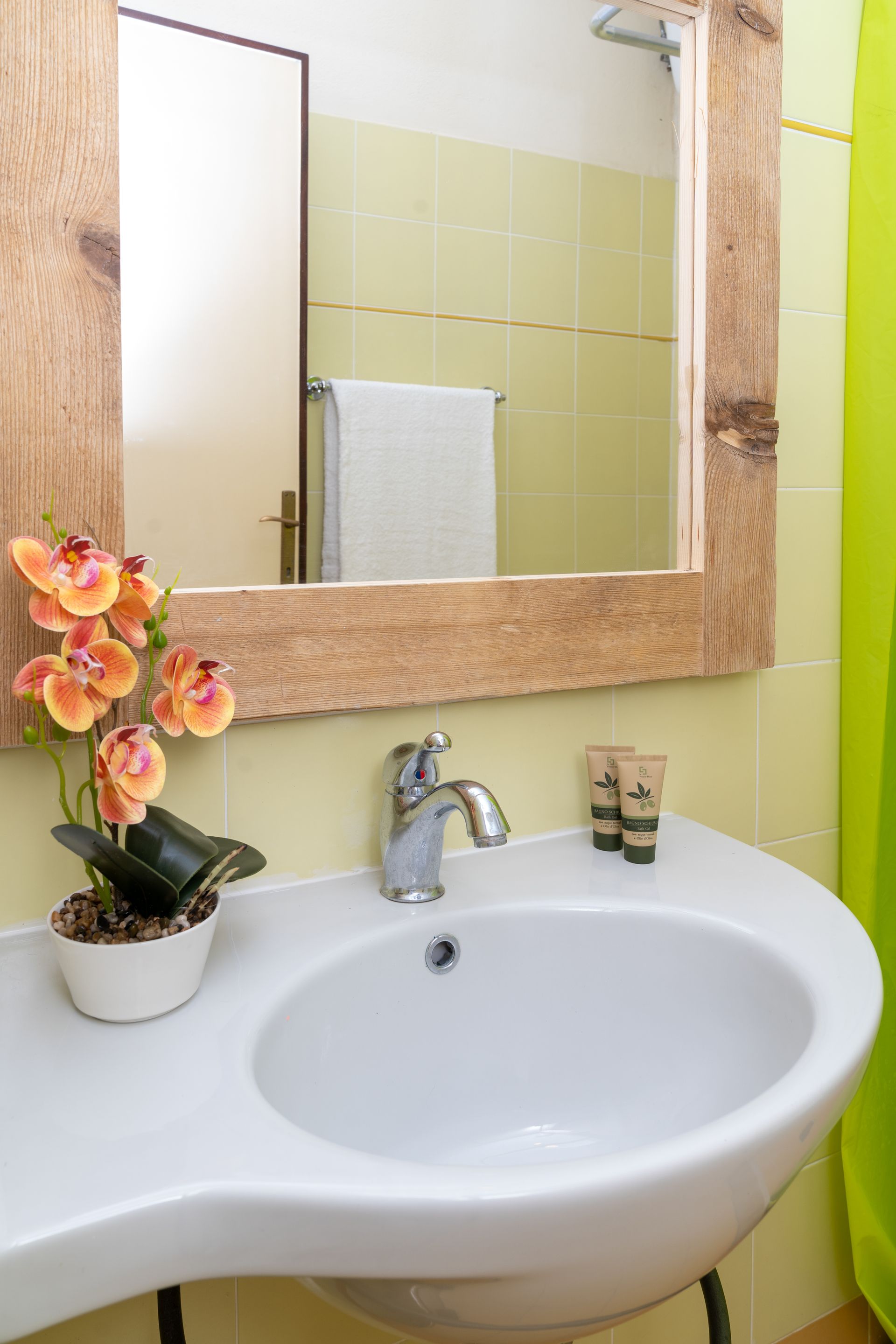Bathroom sink with a wooden framed mirror, flowers, and toiletries on the counter. Light green walls.