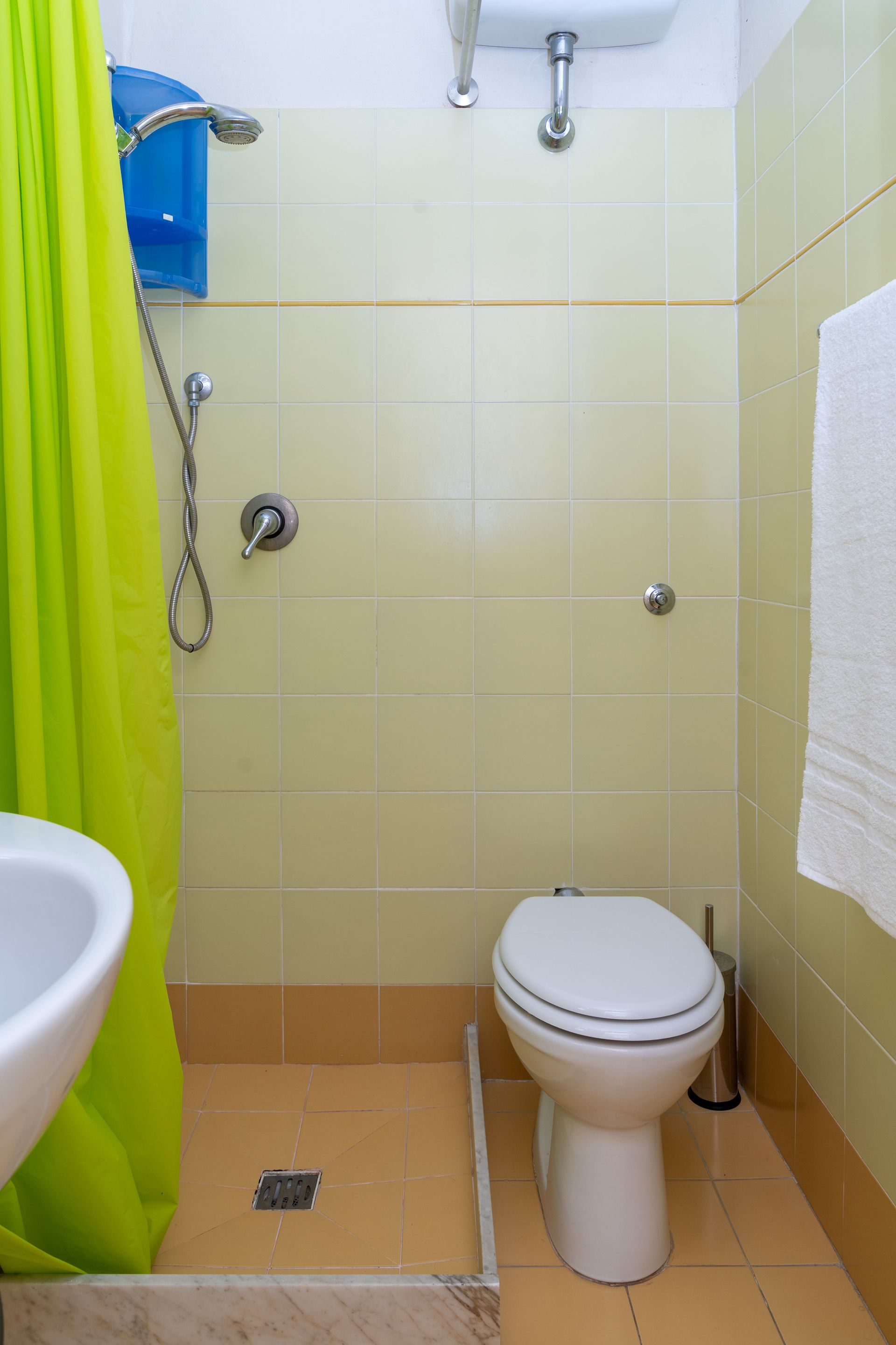 Small bathroom with toilet, shower, sink, and lime-green shower curtain. Light yellow tiled walls and floor.