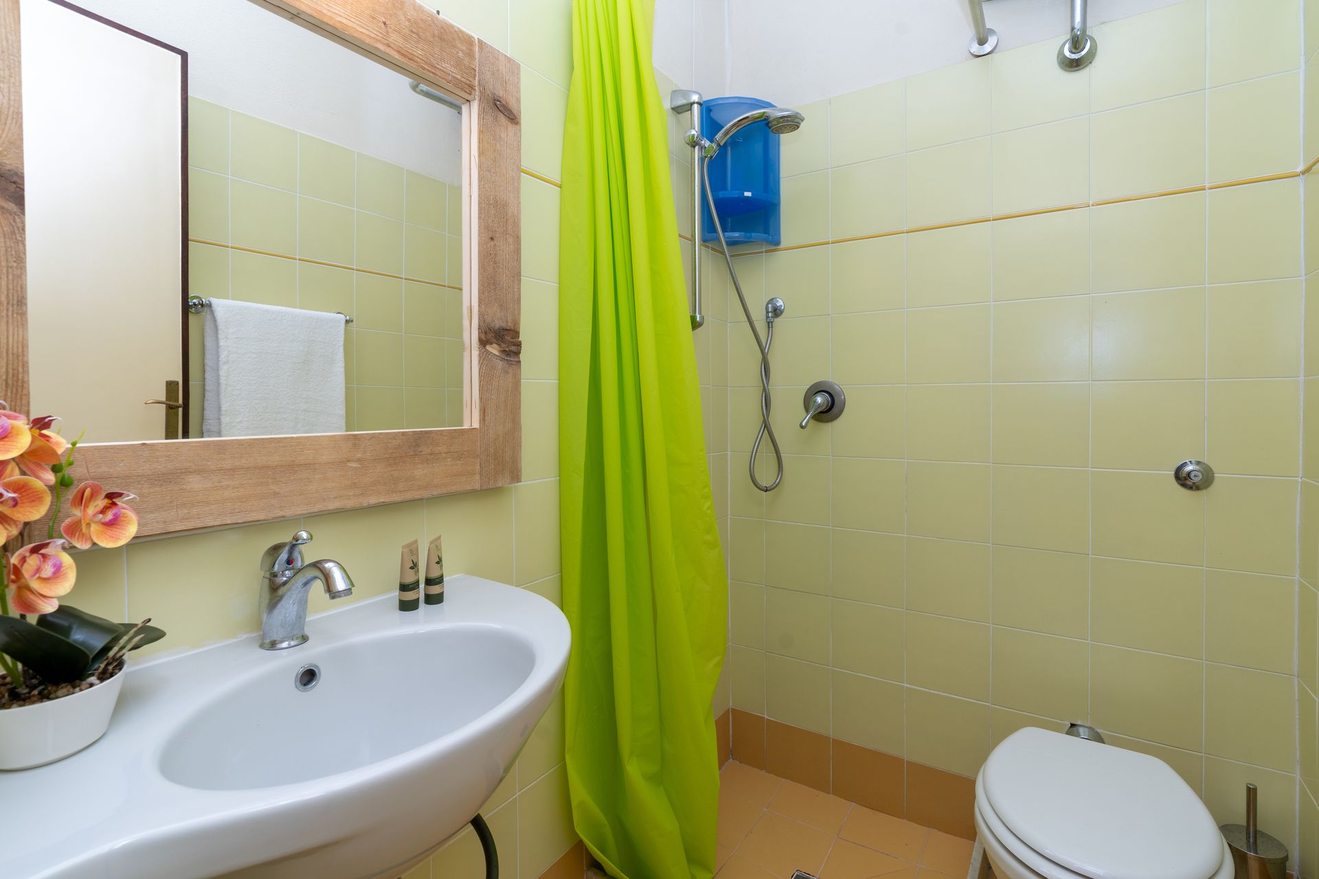 Bathroom with green curtain, white sink, toilet, and beige tile. Rustic mirror frame.
