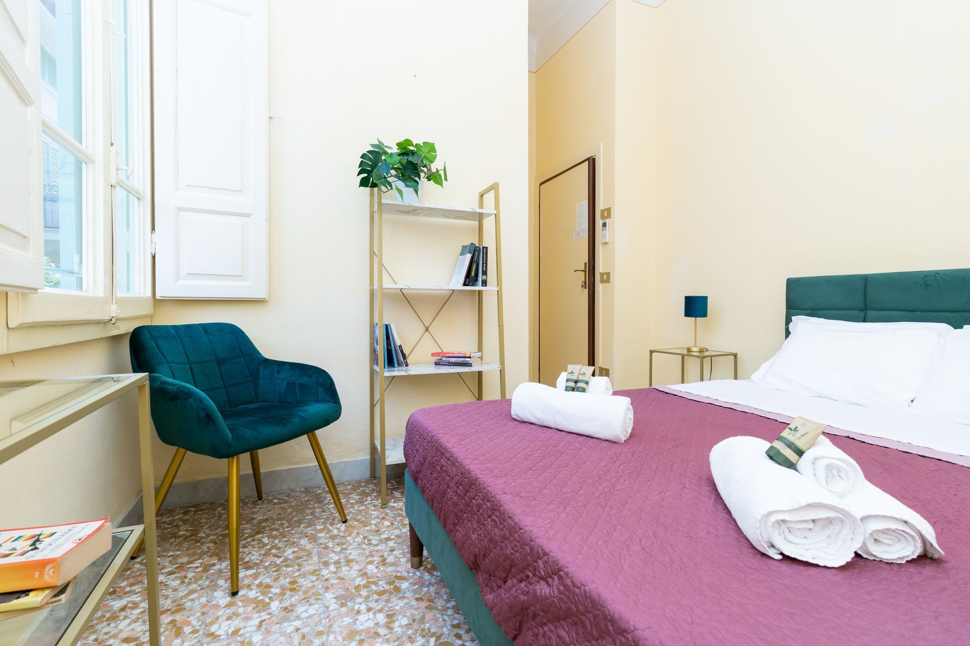 Bedroom with teal chair, gold shelving unit, and a bed with purple cover.