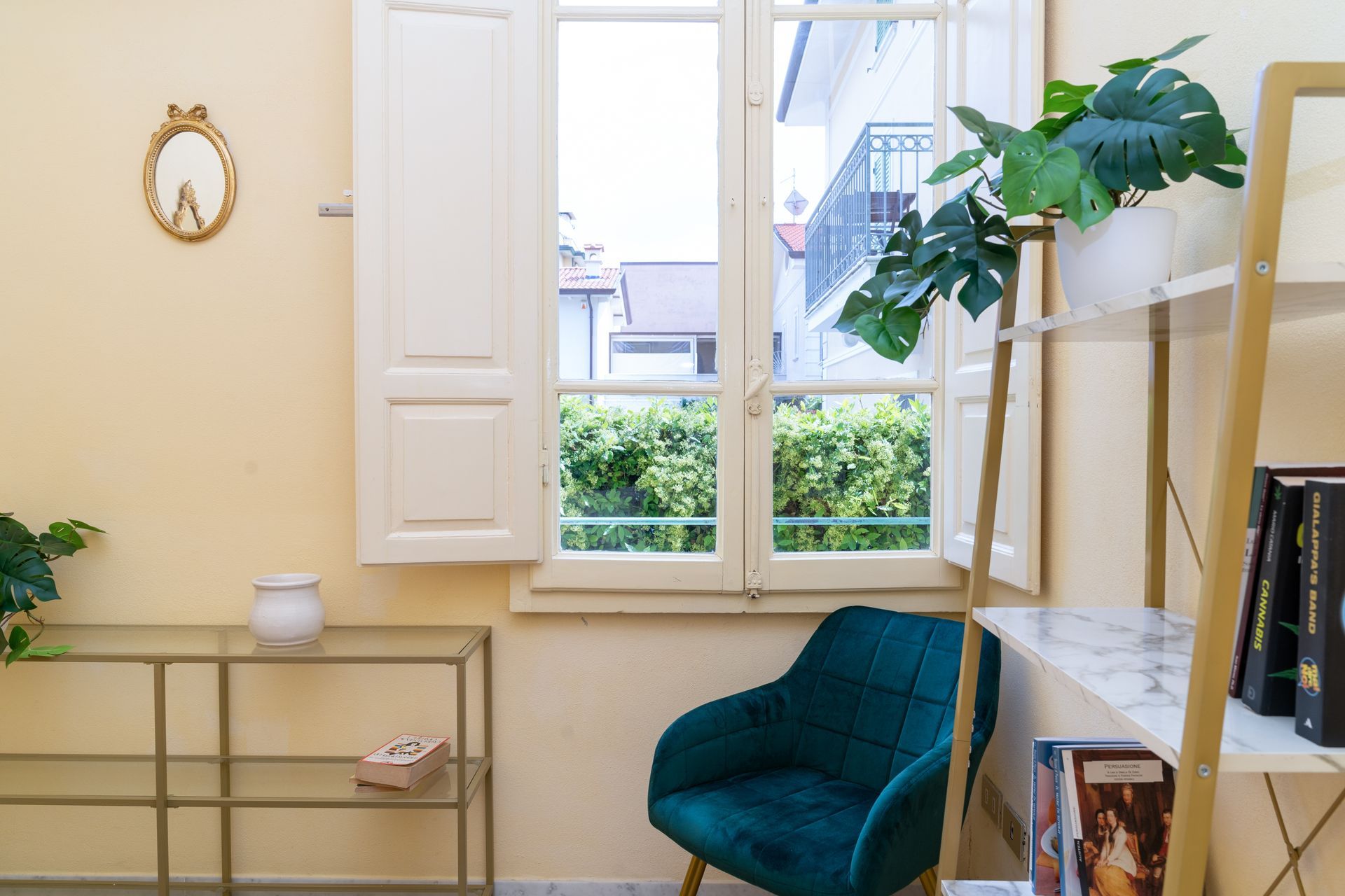 Cozy room with teal armchair, window with white shutters, gold shelving, and decorative plants.