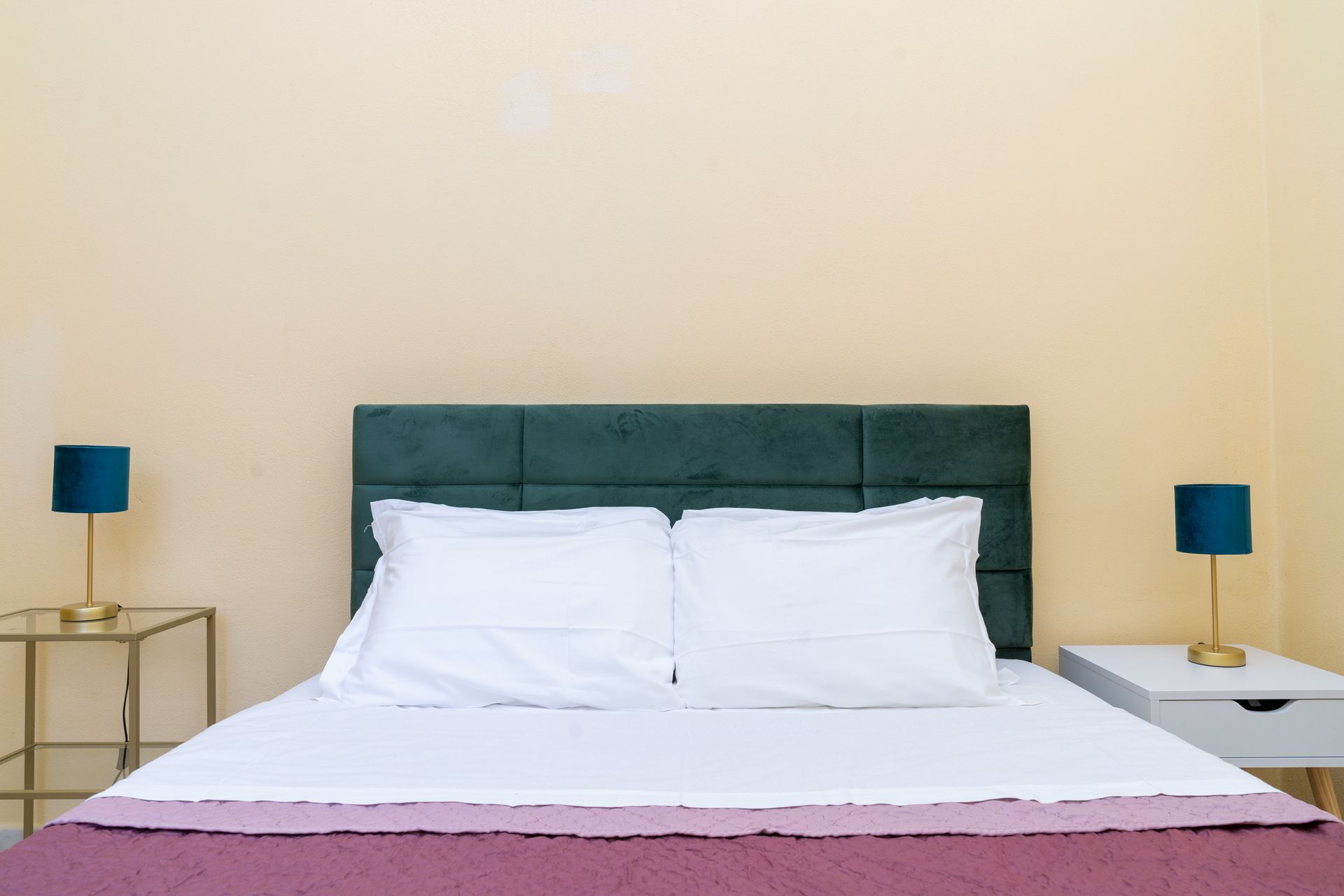 Bed with green headboard, two pillows, purple blanket, two bedside tables, and lamps.