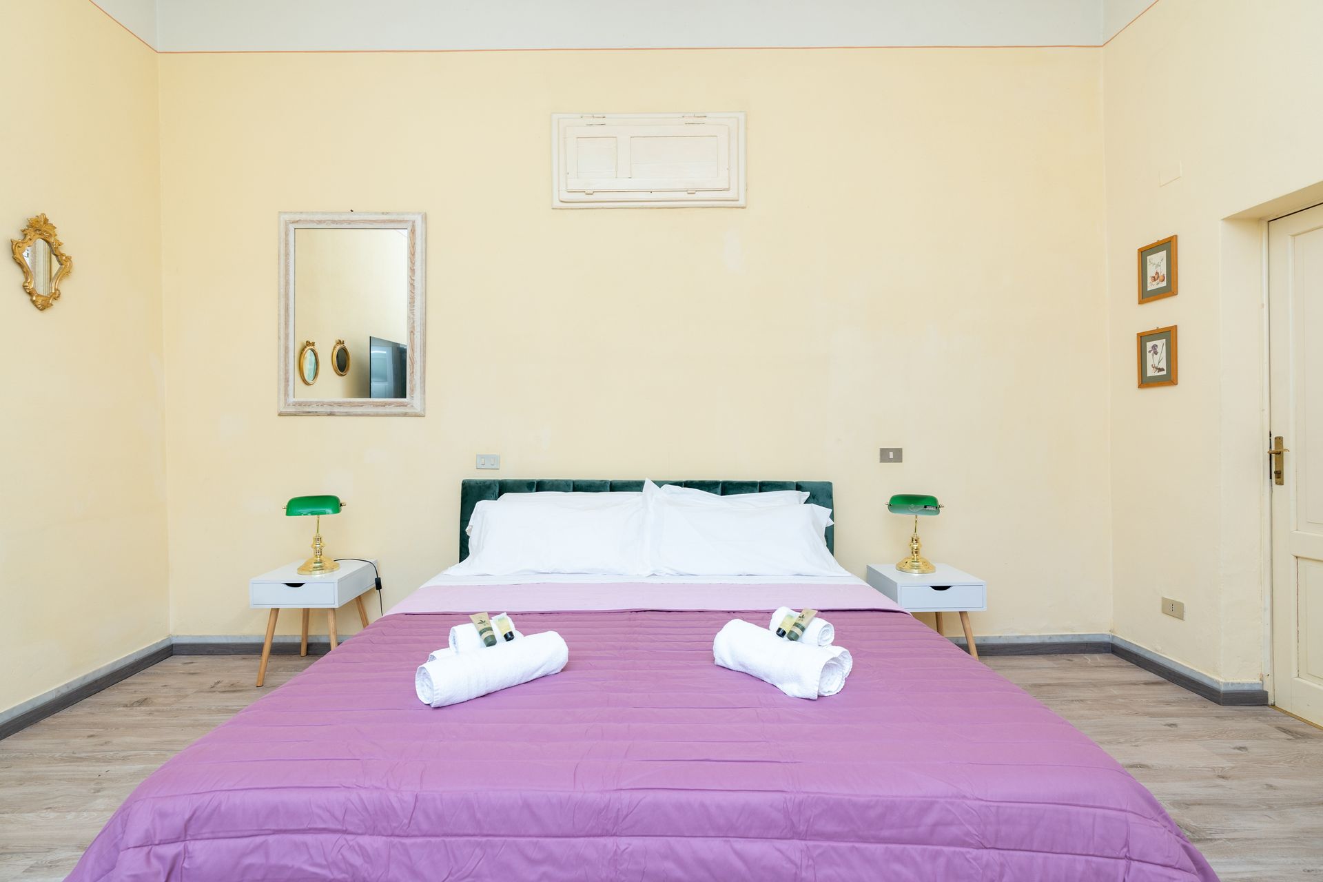 Bedroom with lavender bedding, two white bedside tables, and a mirror.