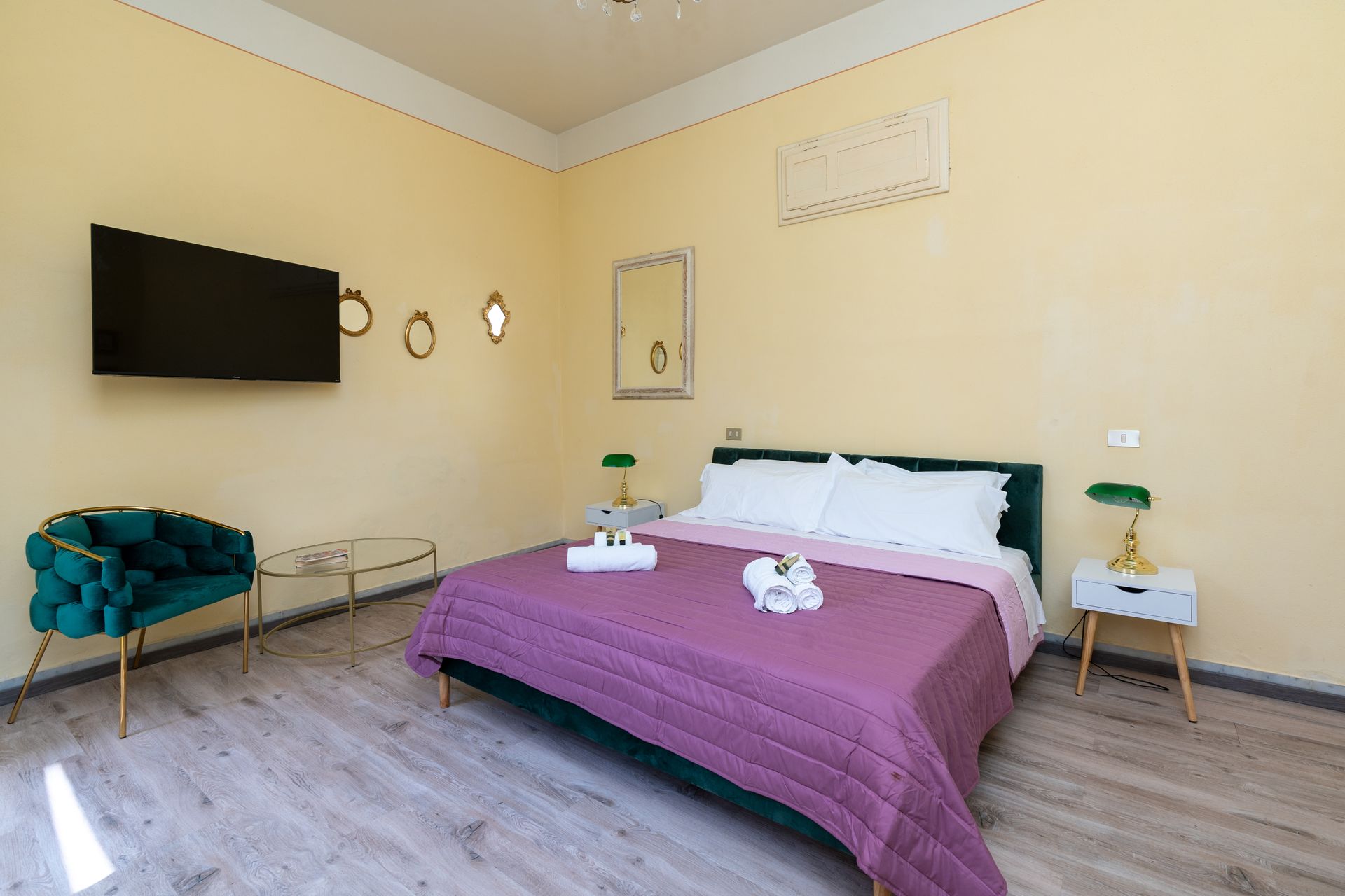 Bedroom with double bed, green chair, TV, bedside tables, and light yellow walls.