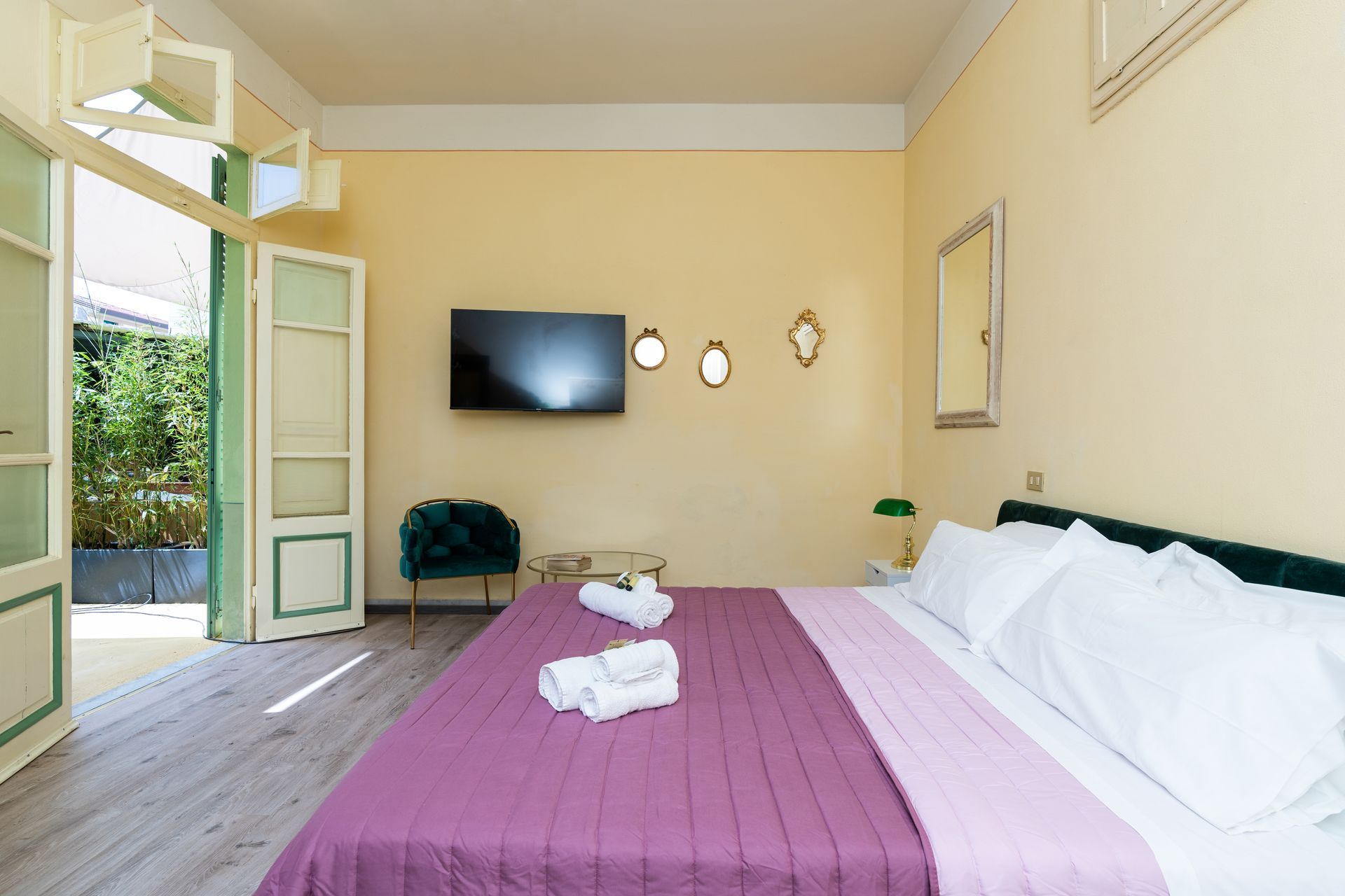 Bedroom with open doors to a patio, featuring a bed, TV, and green armchair.