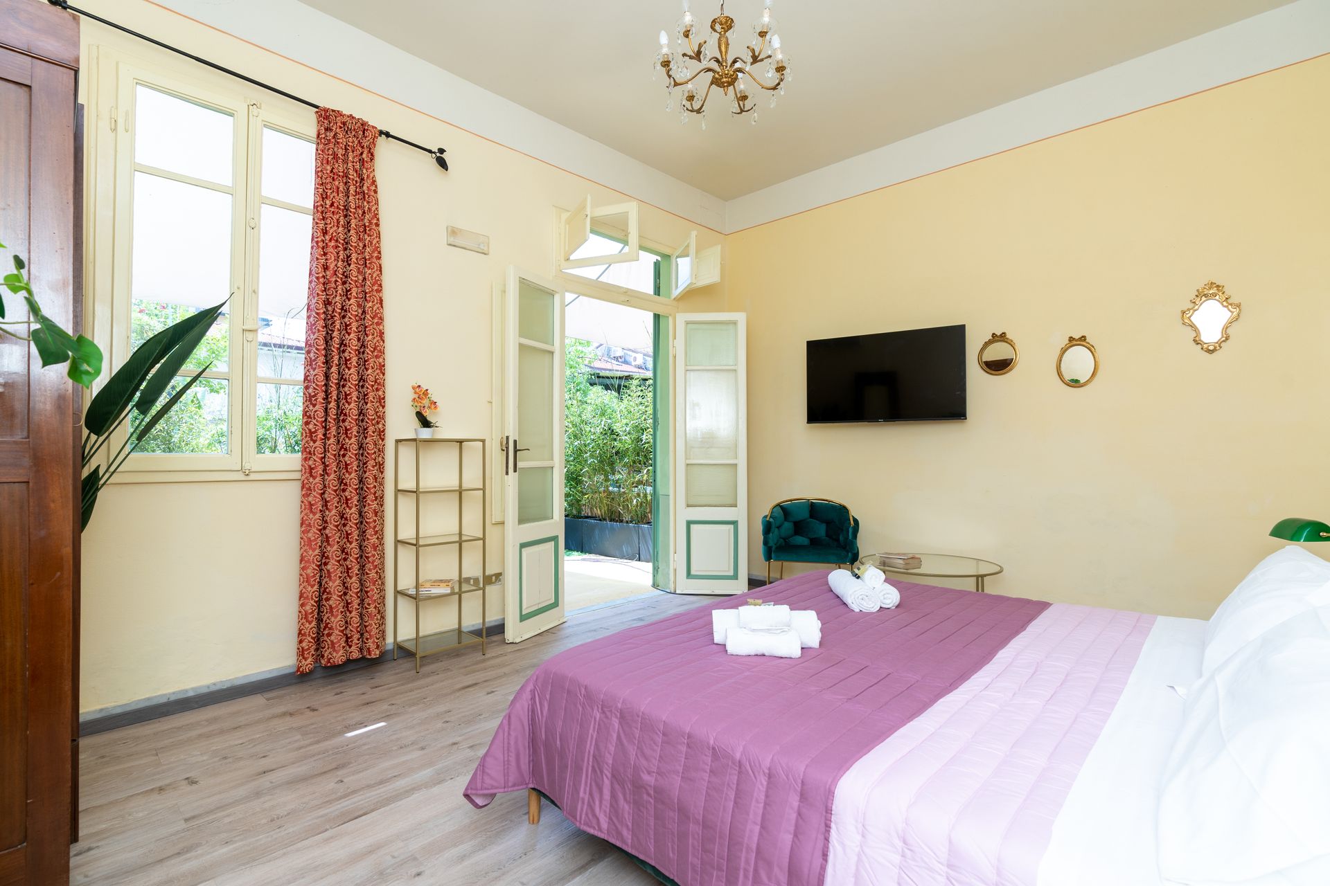 Bedroom with bed, TV, open doors to small patio, light yellow walls, and decorative mirrors.