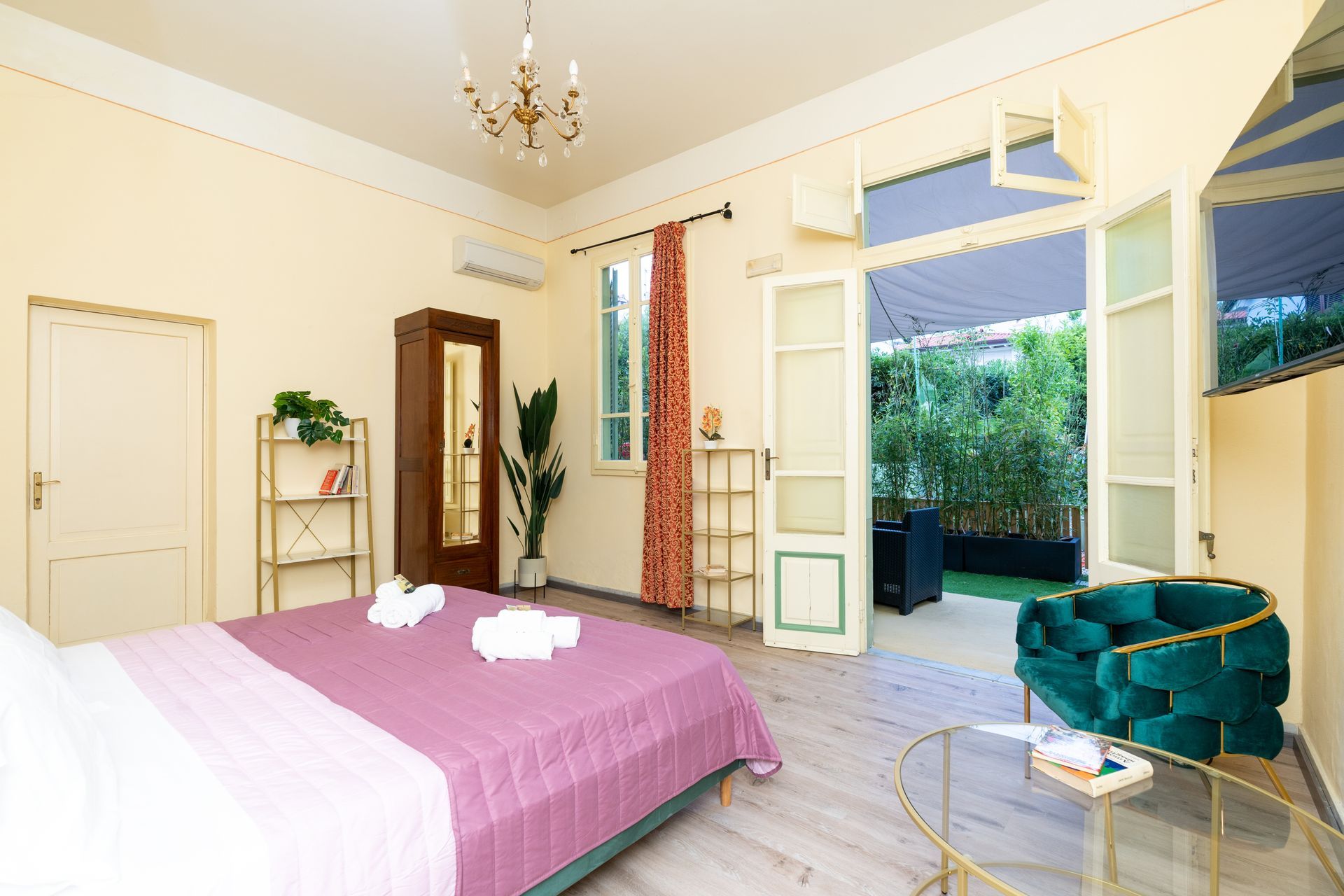 Bedroom with purple bedding, green chair, open doors to patio with plants.
