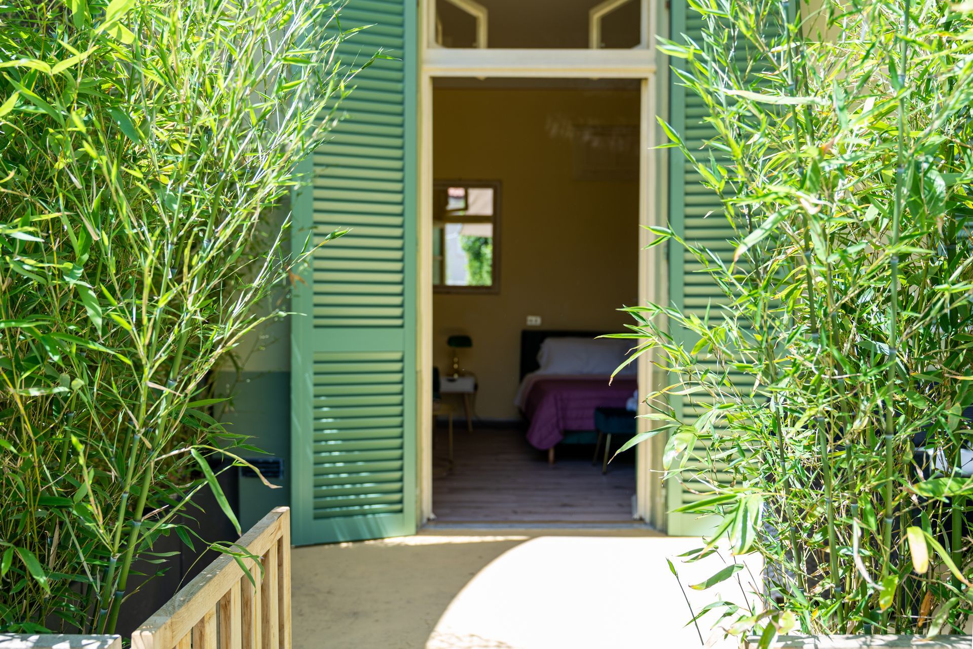 Green shutters open to a bedroom; bamboo plants frame the entrance.