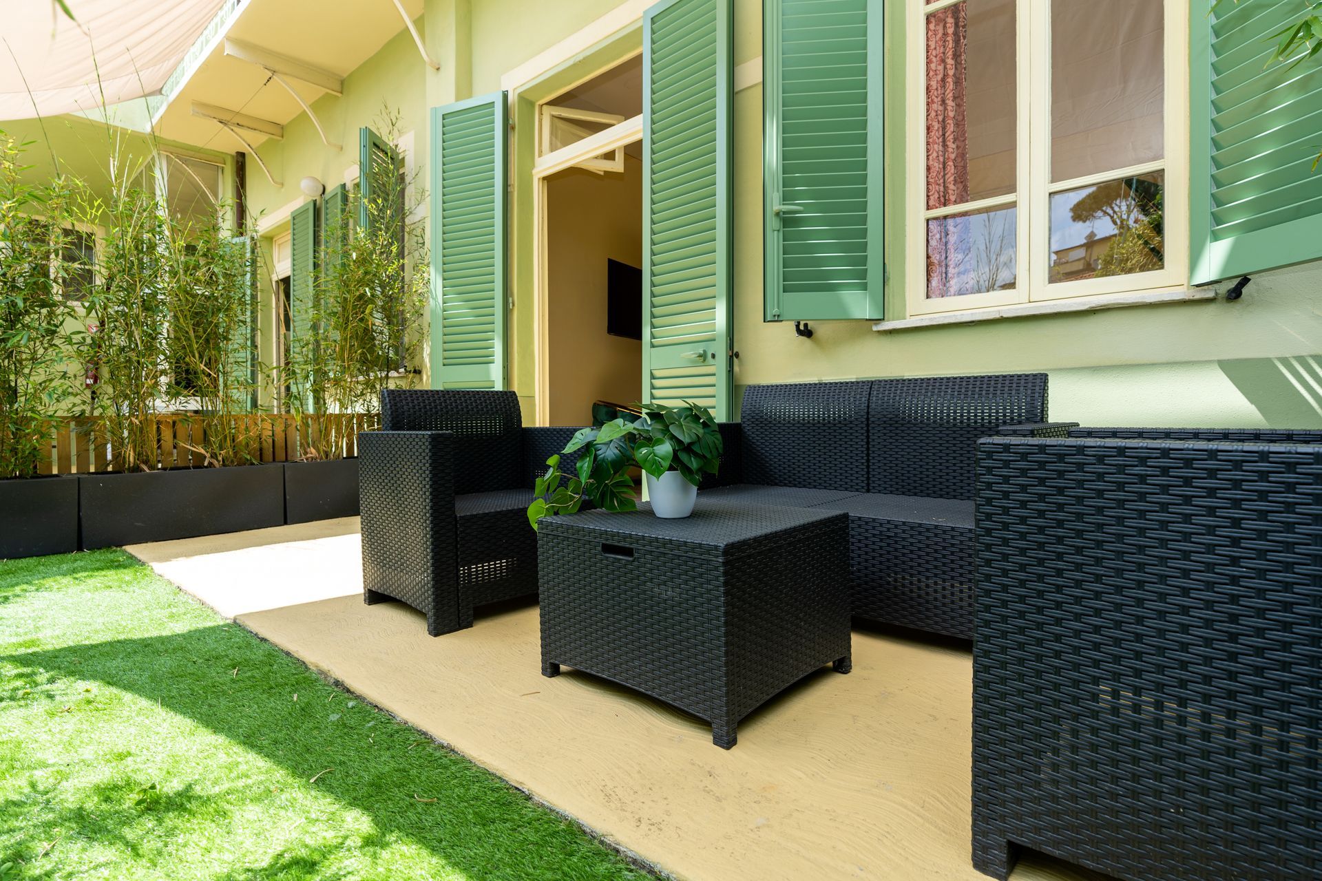 Outdoor seating area with black wicker furniture on a concrete patio, green shutters, and a lawn.