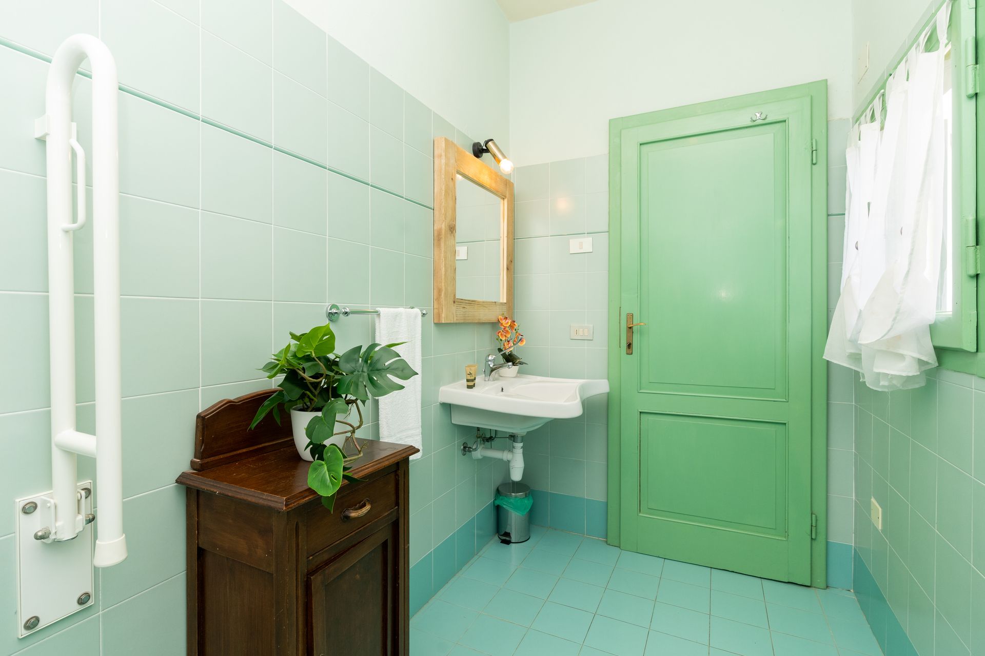 Light green bathroom with a grab bar, vanity, and a green door.