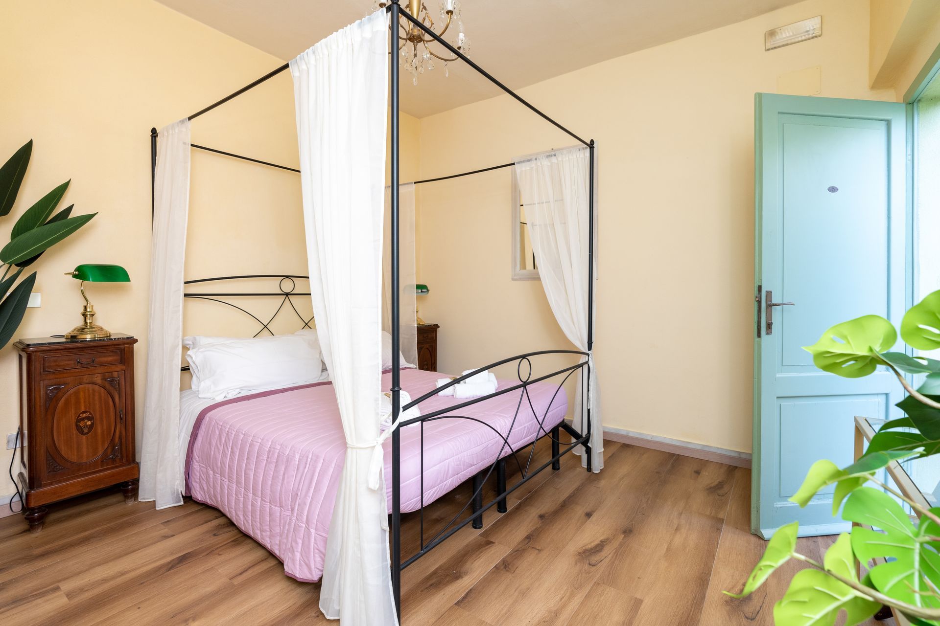 Bedroom with canopy bed, pink bedding, wooden floors, and a light blue door.