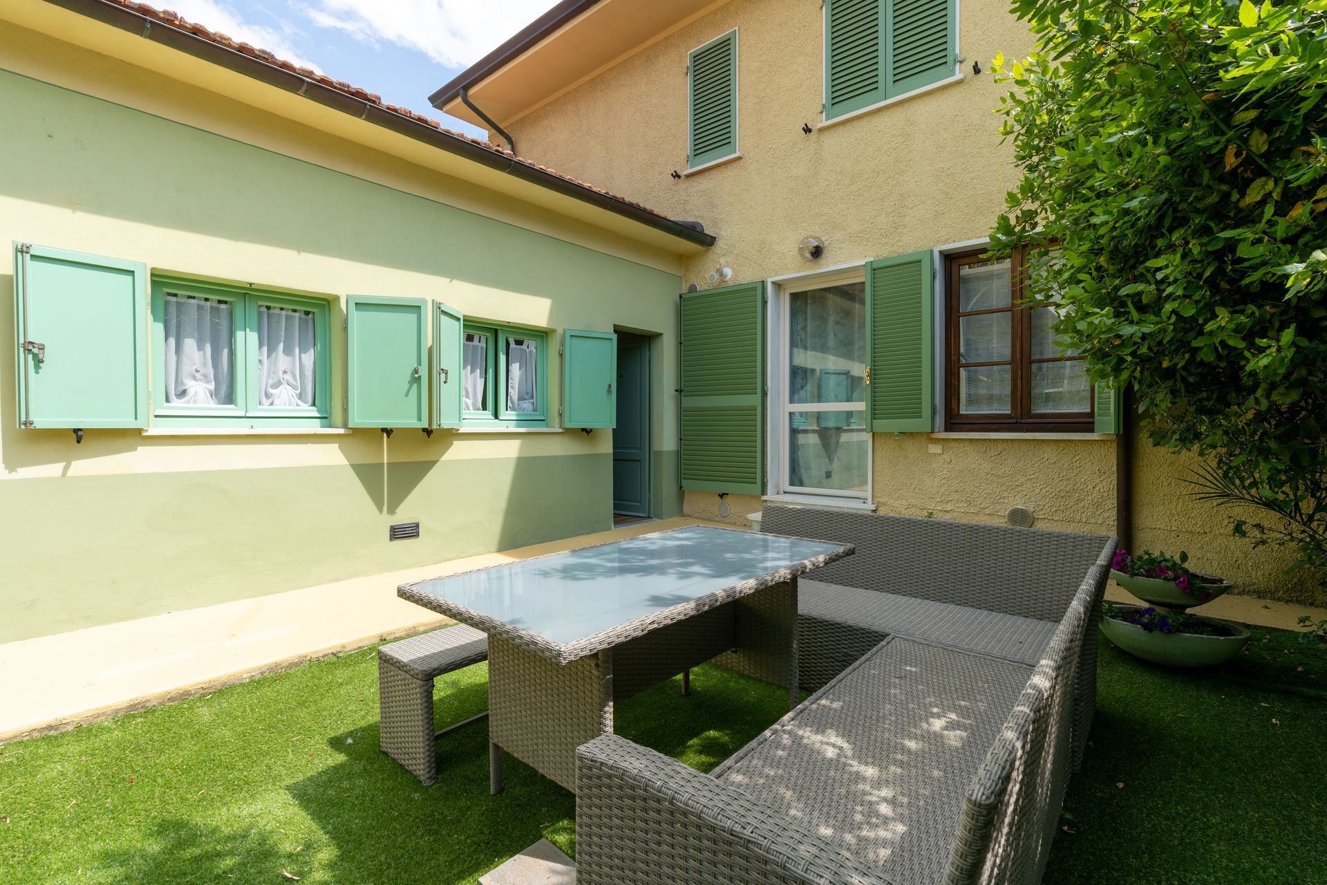 Exterior patio with a table and bench seating in front of a house with green shutters.