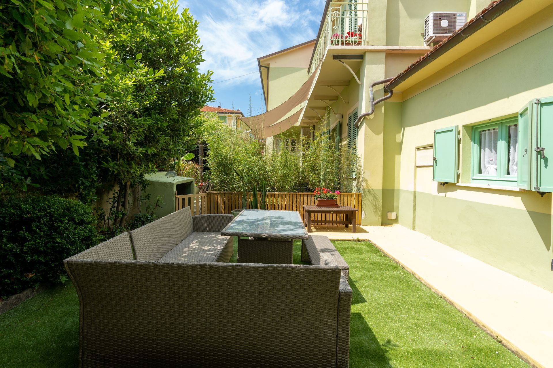 Outdoor patio with wicker furniture, green lawn, and building with shutters.