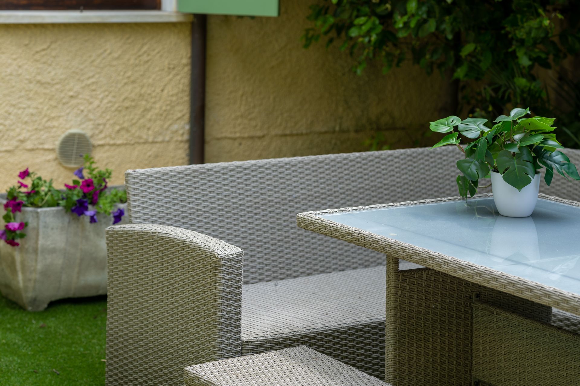 Outdoor seating area with a wicker sofa, table, and potted flowers.