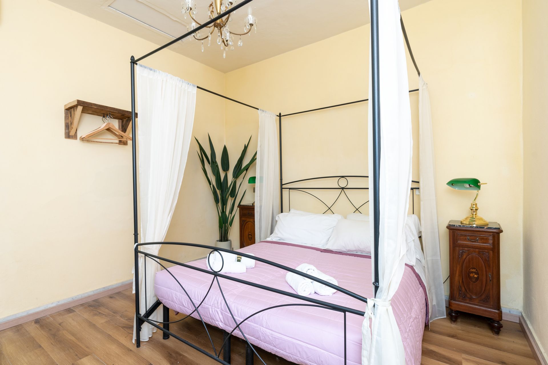 Bedroom with a four-poster bed, white curtains, and a nightstand with a lamp.