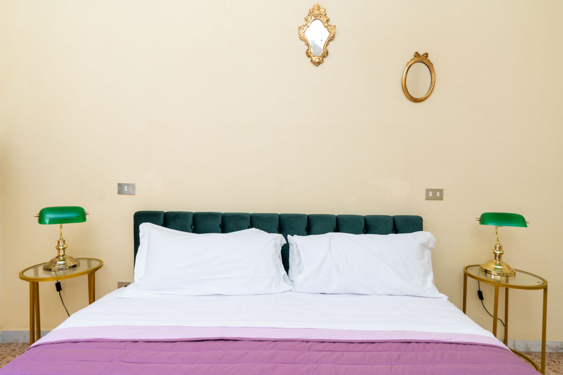 Bedroom with a green headboard, white bedding, purple blanket, two gold side tables with green lamps.