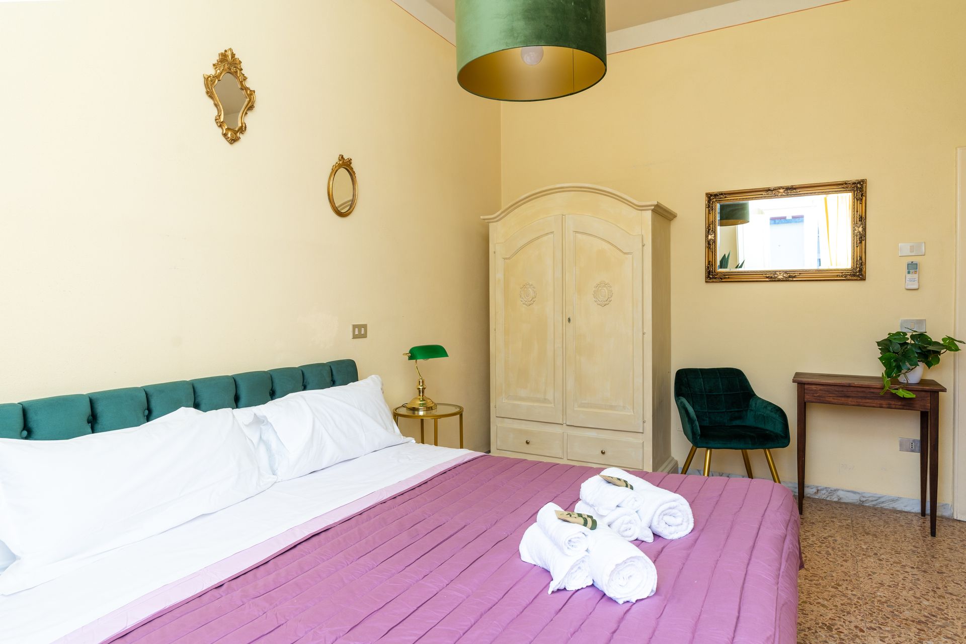 Bedroom with a large bed, wardrobe, green velvet chair, and decorative mirrors.