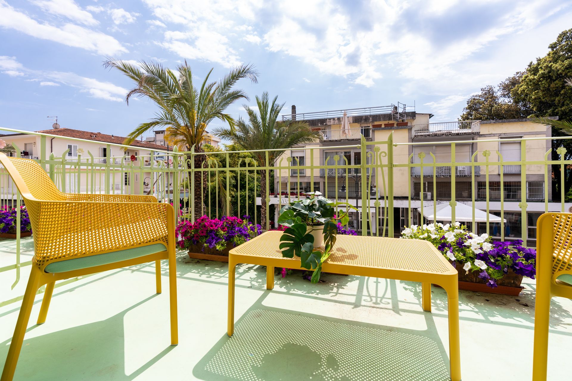 Yellow patio furniture on a balcony with potted flowers and city views.