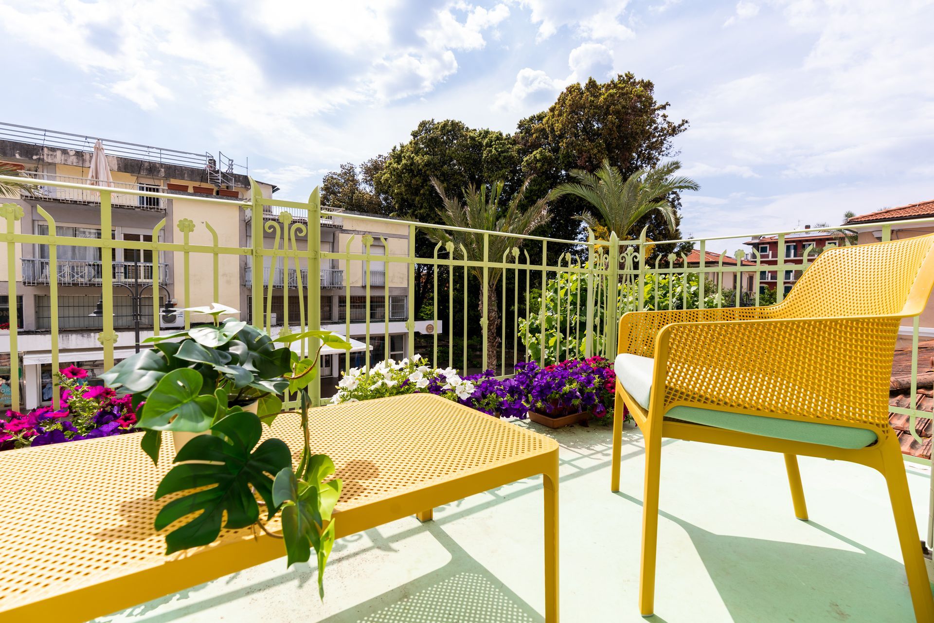 Yellow outdoor furniture on a balcony with flowers and a view of buildings and trees.